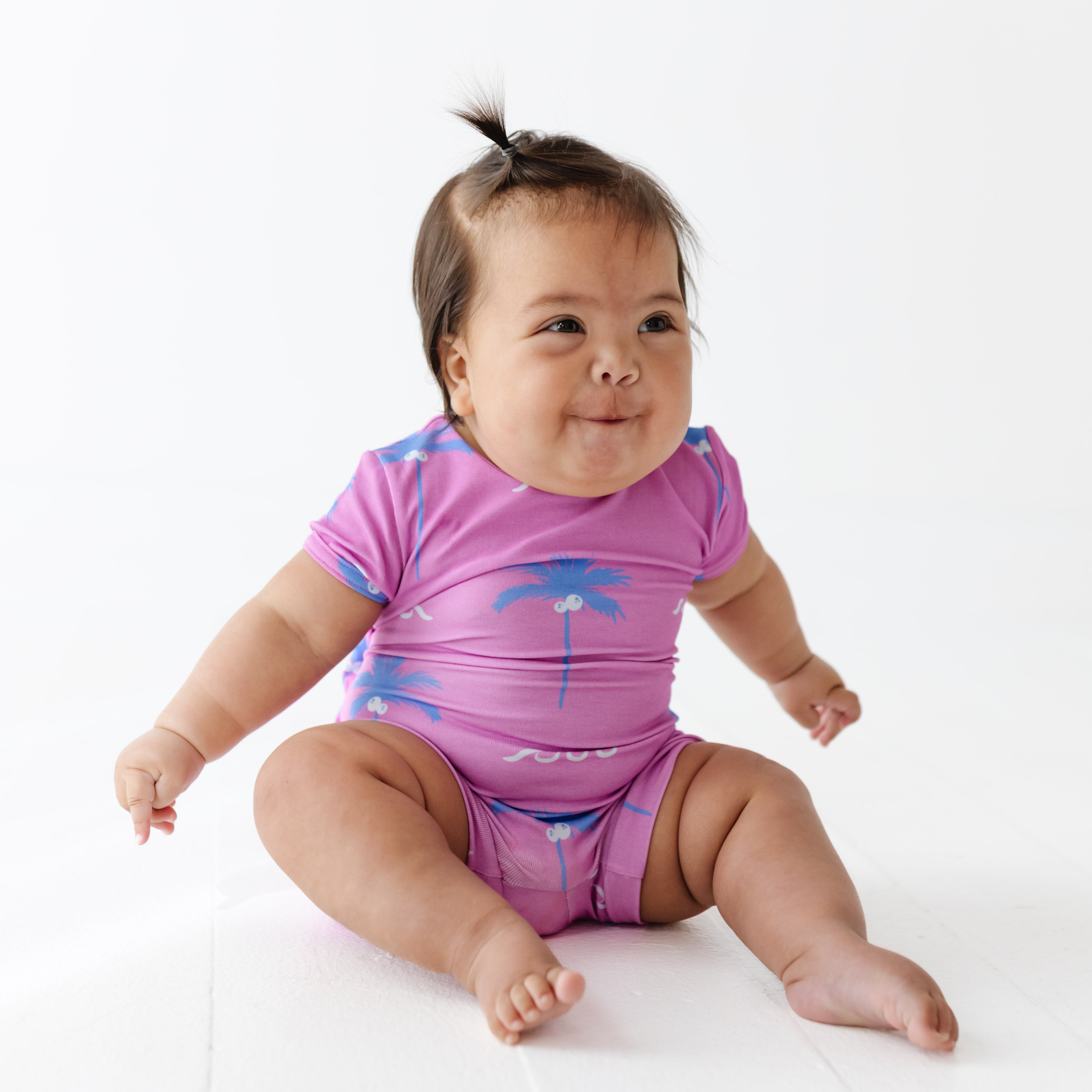 Baby wearing a pink onesie with blue palm tree design on a white background