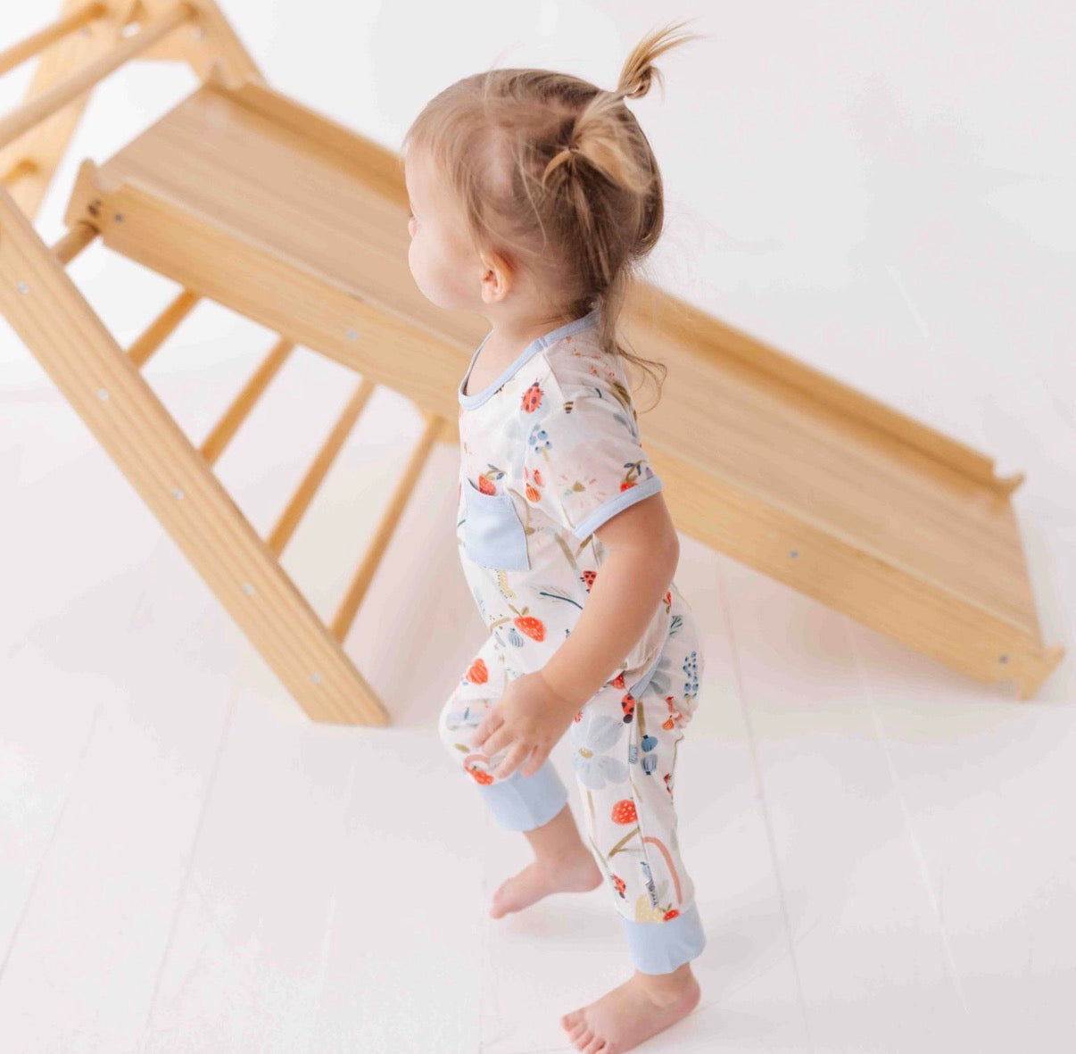 Child wearing a patterned outfit standing next to a wooden toy.