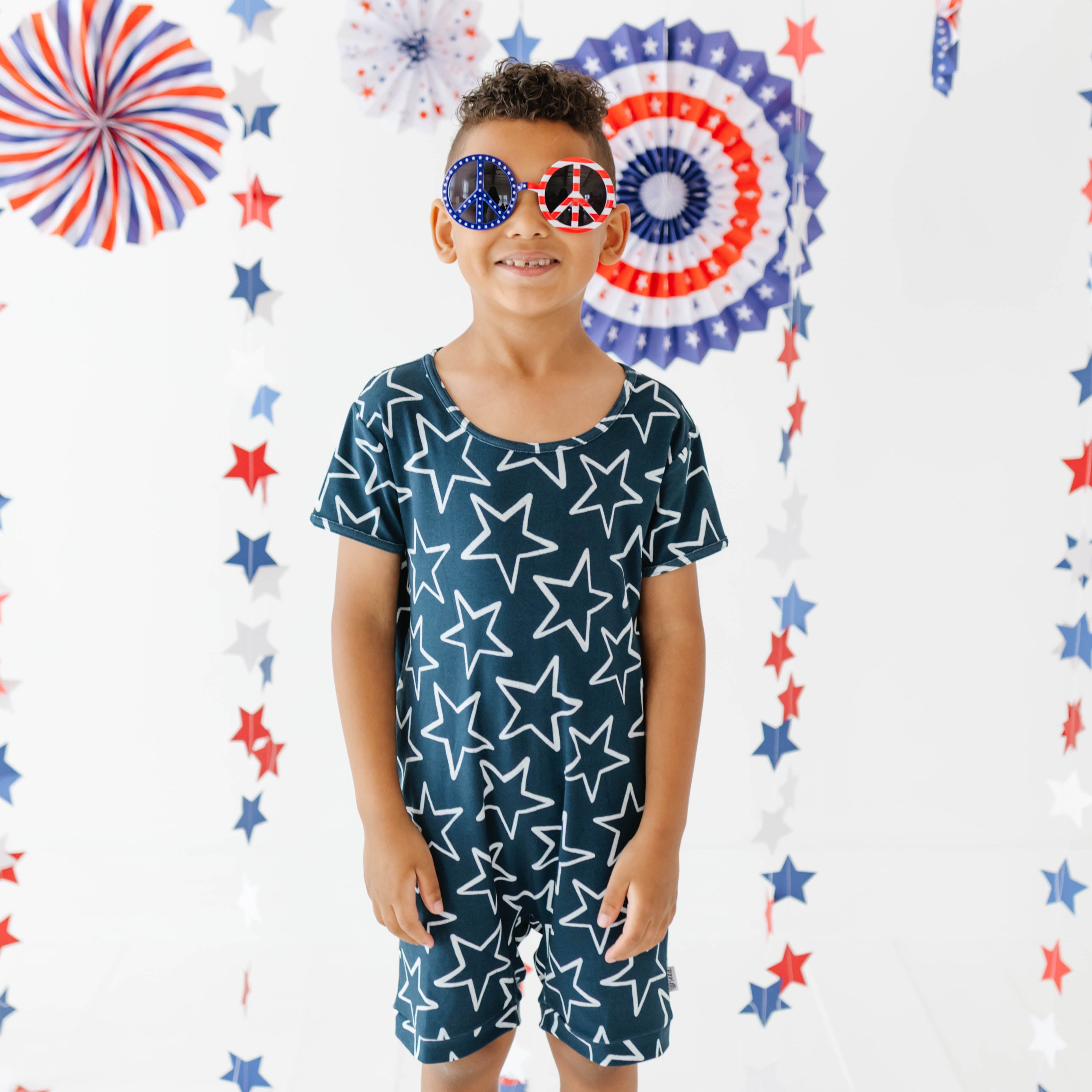 Child wearing a blue star-patterned outfit with red, white, and blue decorations in the background.