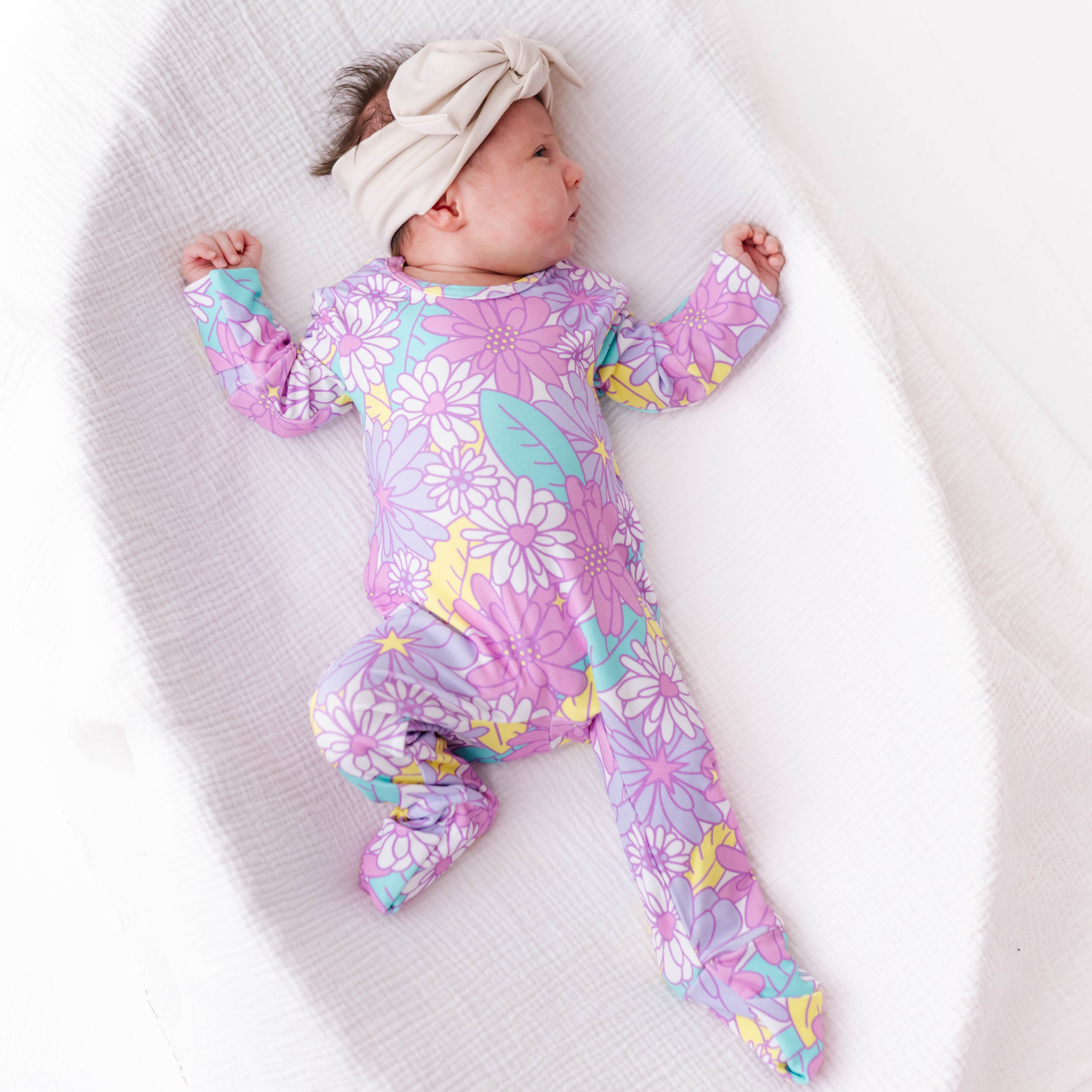 Baby wearing a colorful floral onesie lying on a white blanket