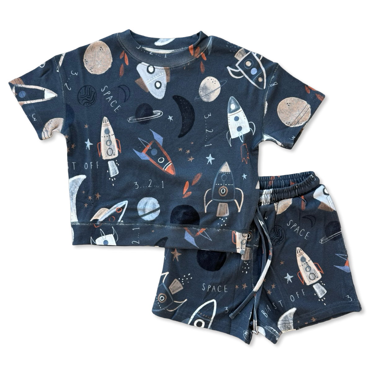 A two-piece kids' pajama set featuring a short-sleeve top and matching shorts in dark navy blue with a playful space-themed print of rockets, planets, moons, stars, and the words 'SPACE' and 'SET OFF'.