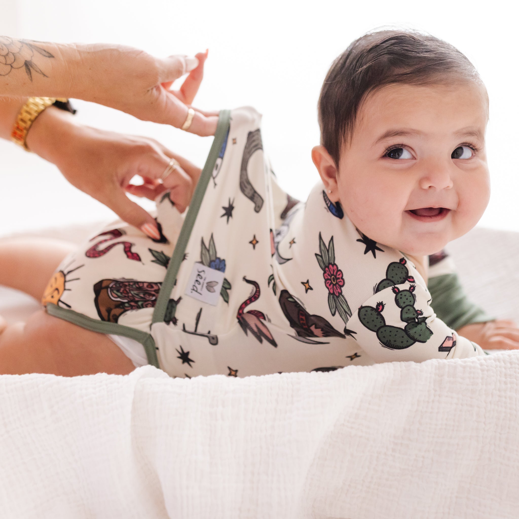 Baby wearing a bib with animal prints, sitting on a white surface.