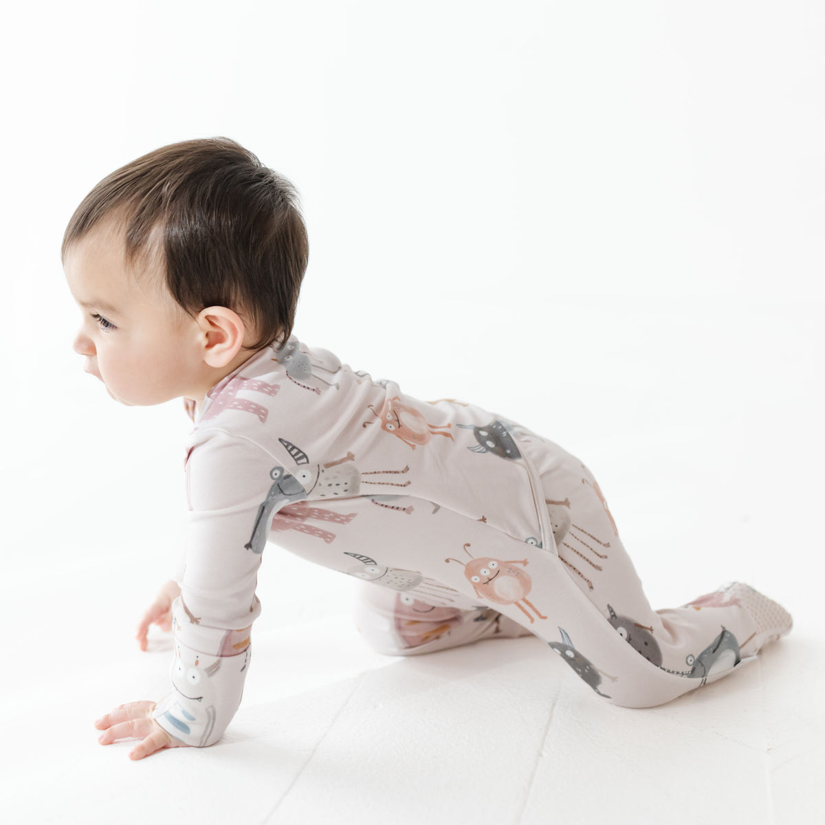 Baby in a patterned onesie sitting on a white surface