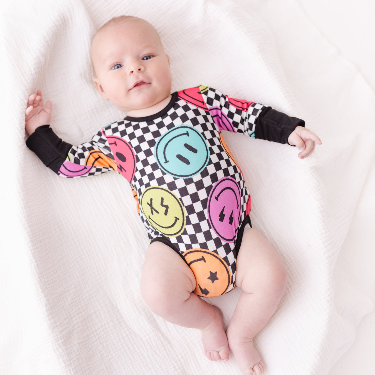 Baby wearing a colorful onesie with smiley face patterns on a white blanket