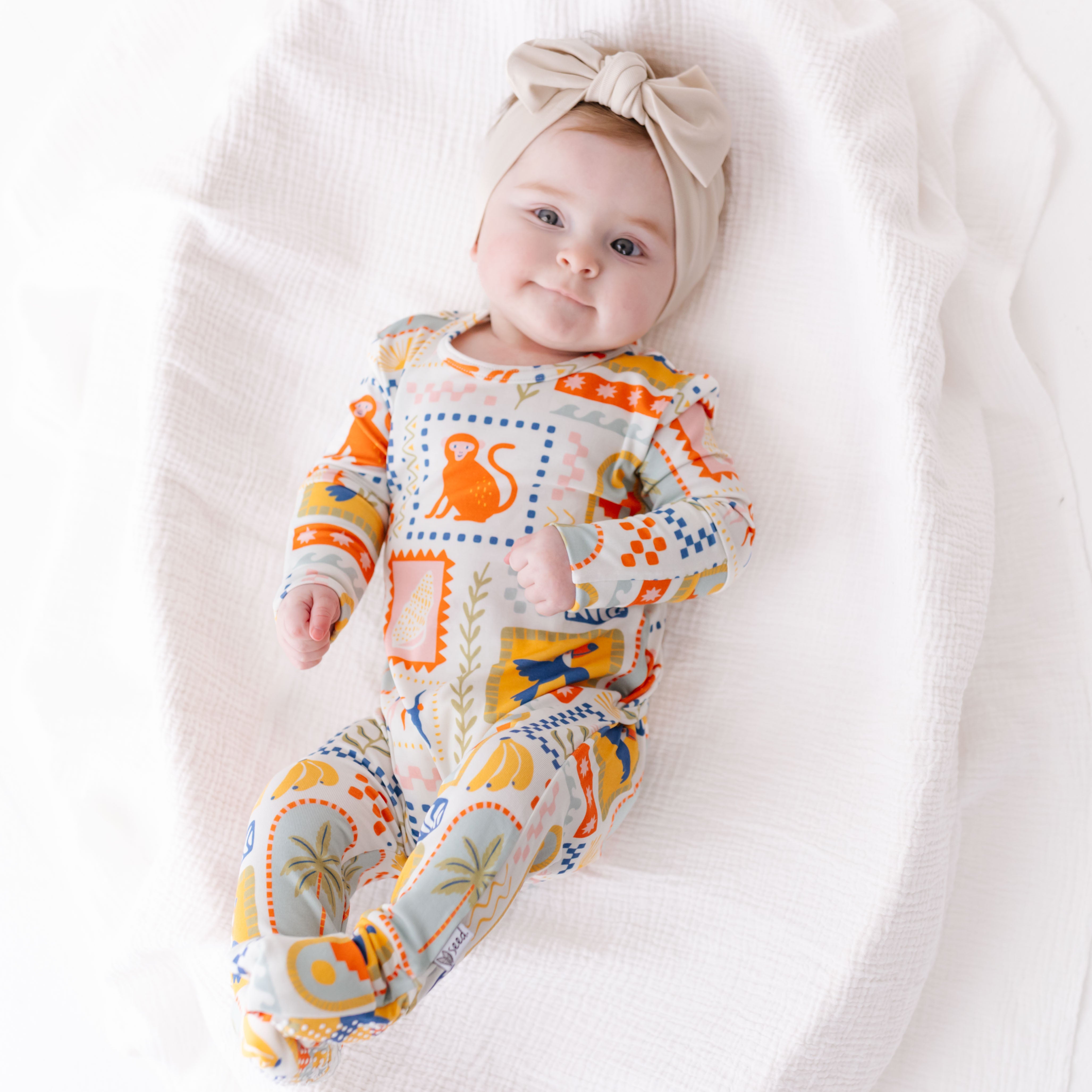 Baby wearing a colorful onesie with a pattern of orange and blue shapes on a white background