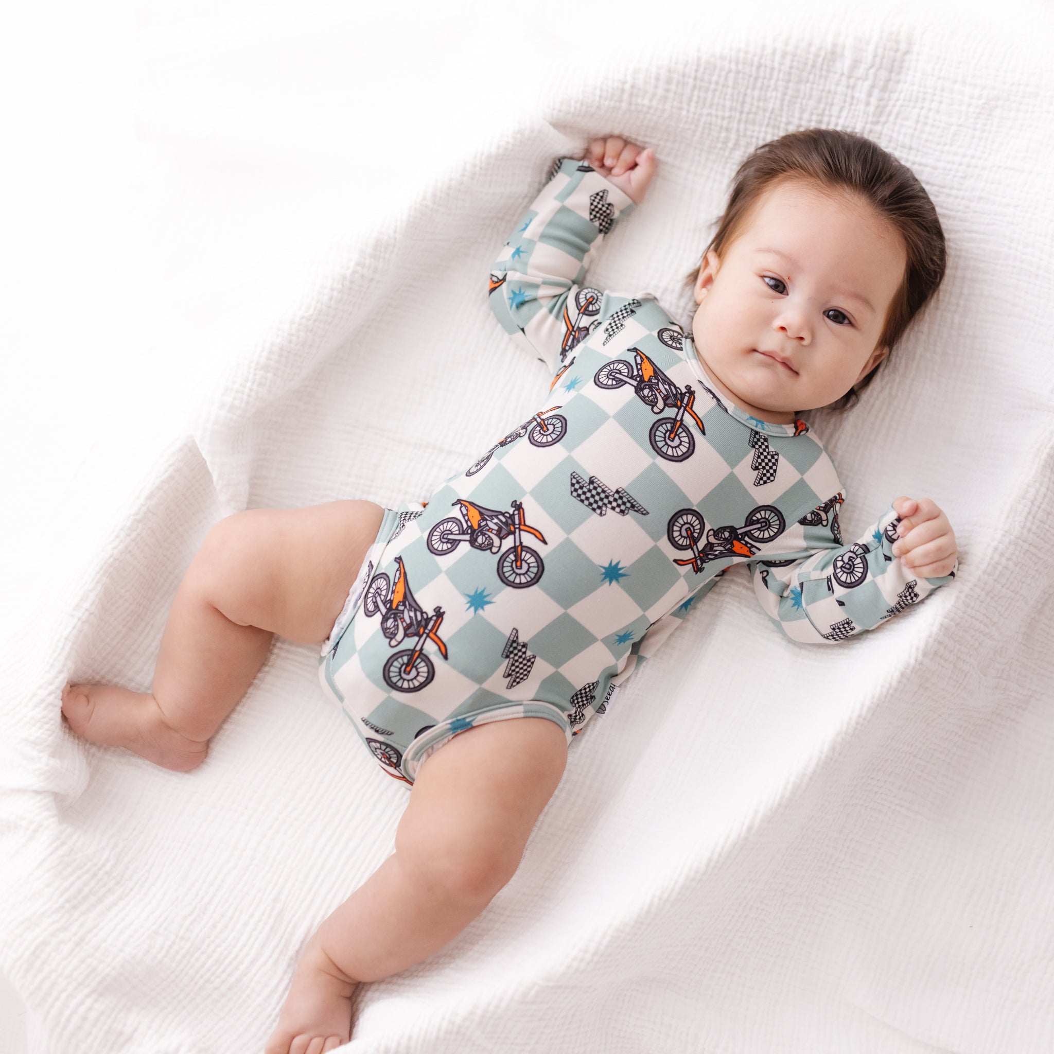 Baby lying on a white blanket wearing a patterned onesie.