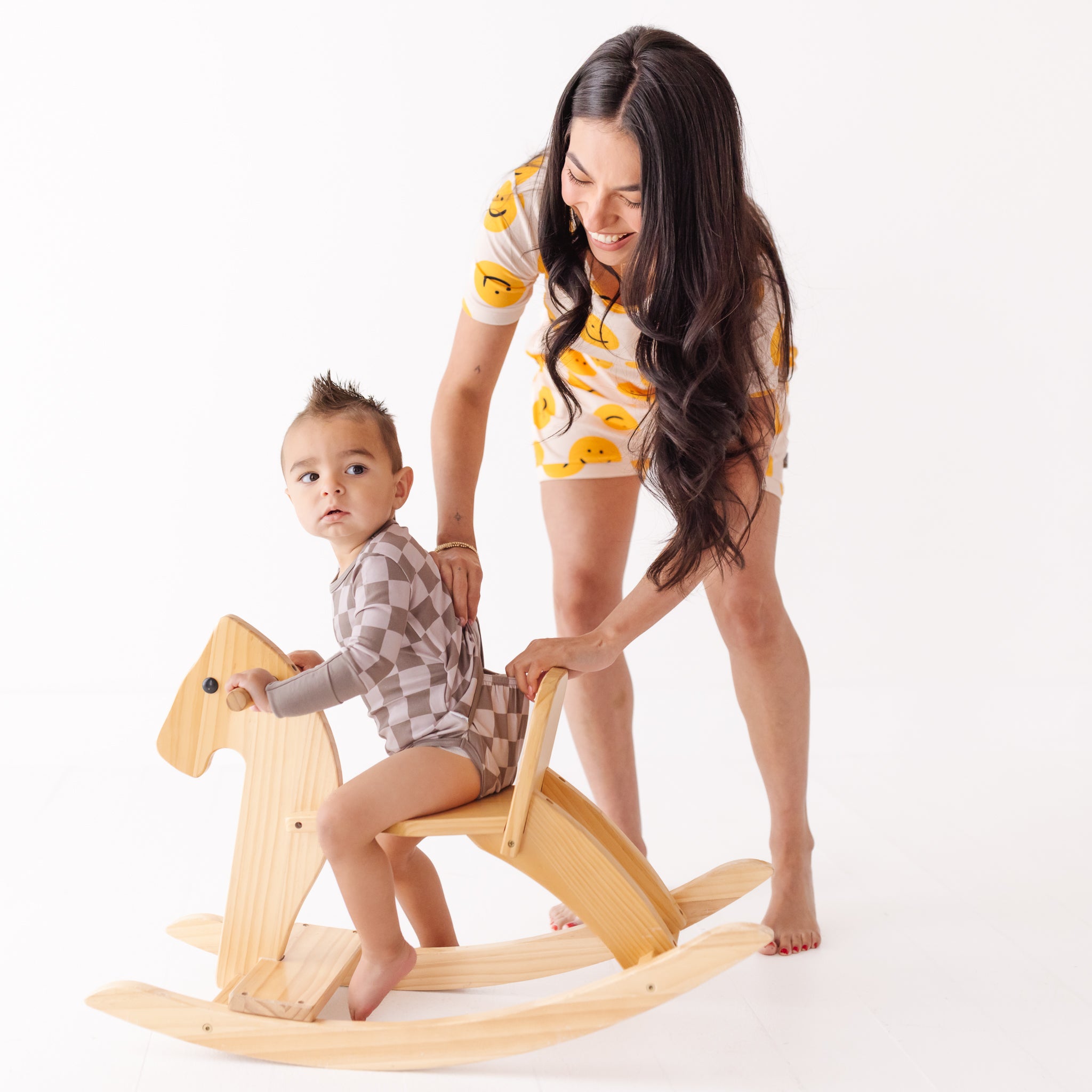 Woman assisting a child on a wooden rocking horse against a white background