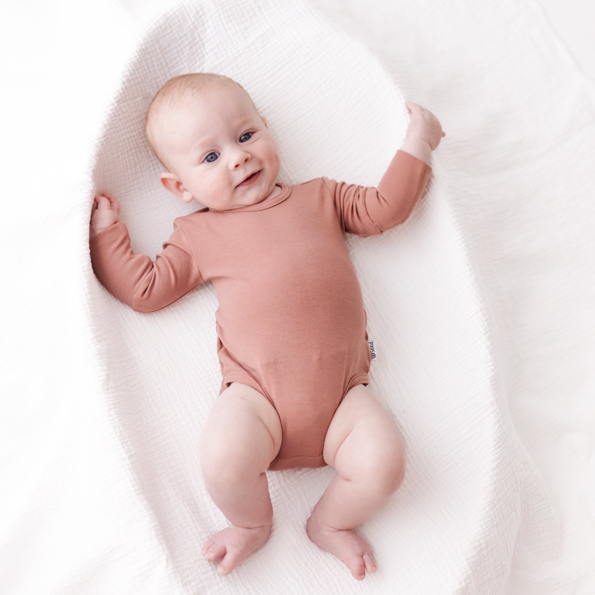 Baby in a pink onesie lying on a white blanket
