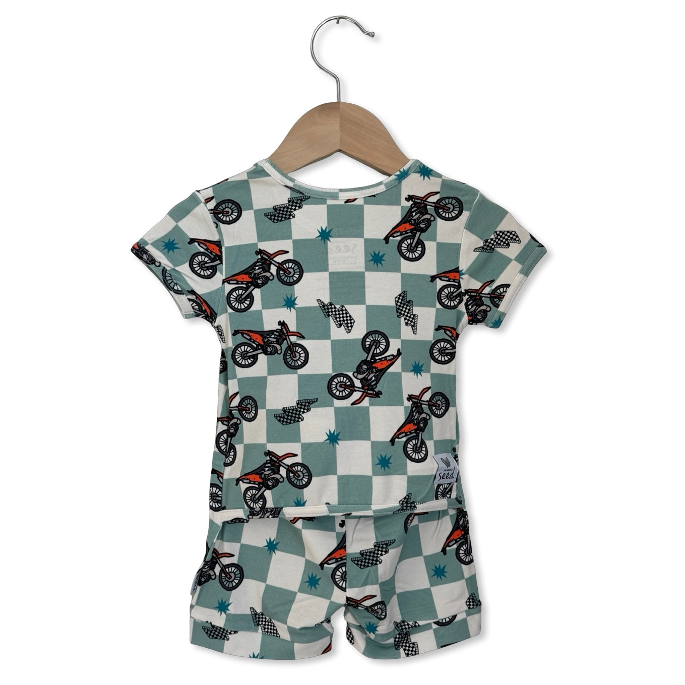 Children's outfit with dirt bike pattern on a checkered background, hanging on a wooden hanger.