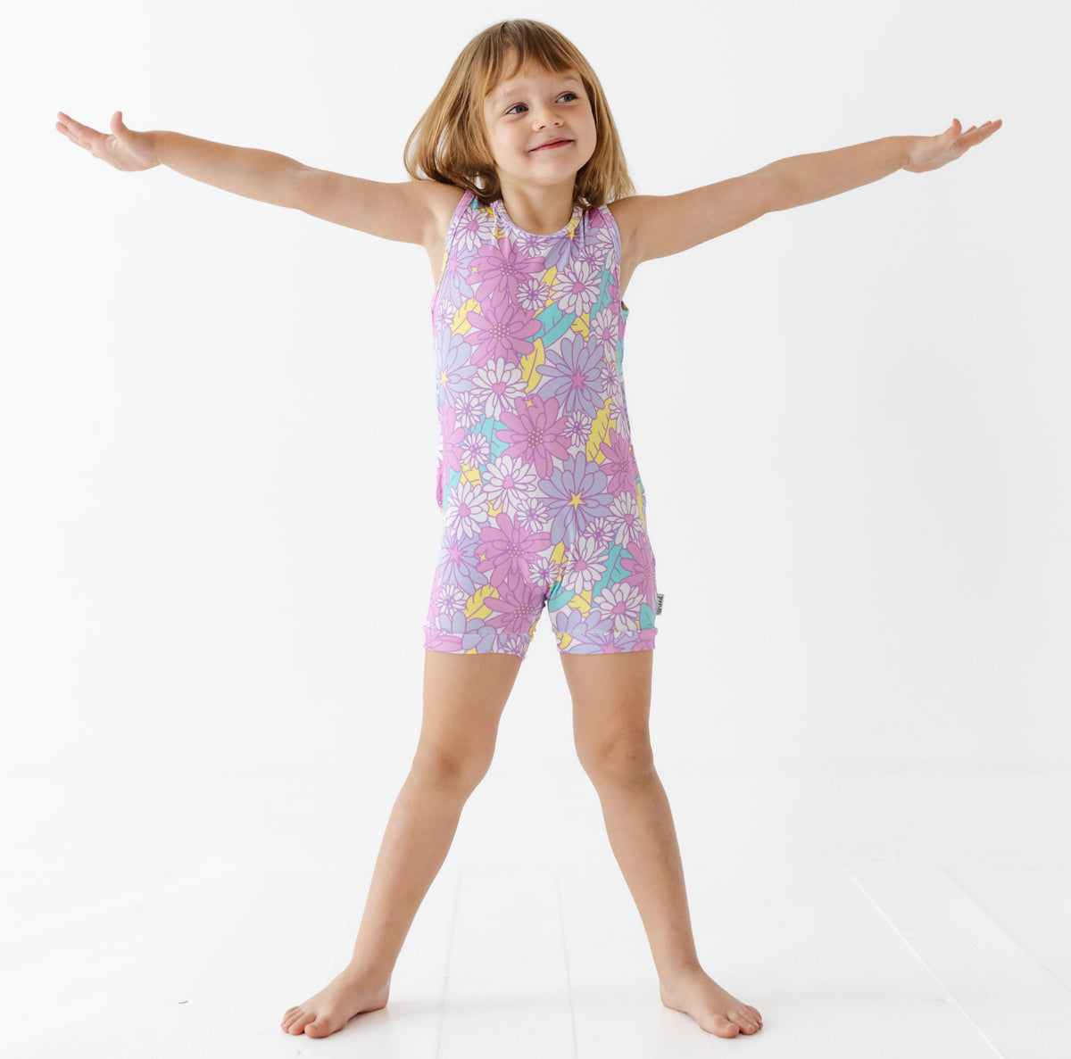 Child wearing a colorful floral romper with arms outstretched on a white background