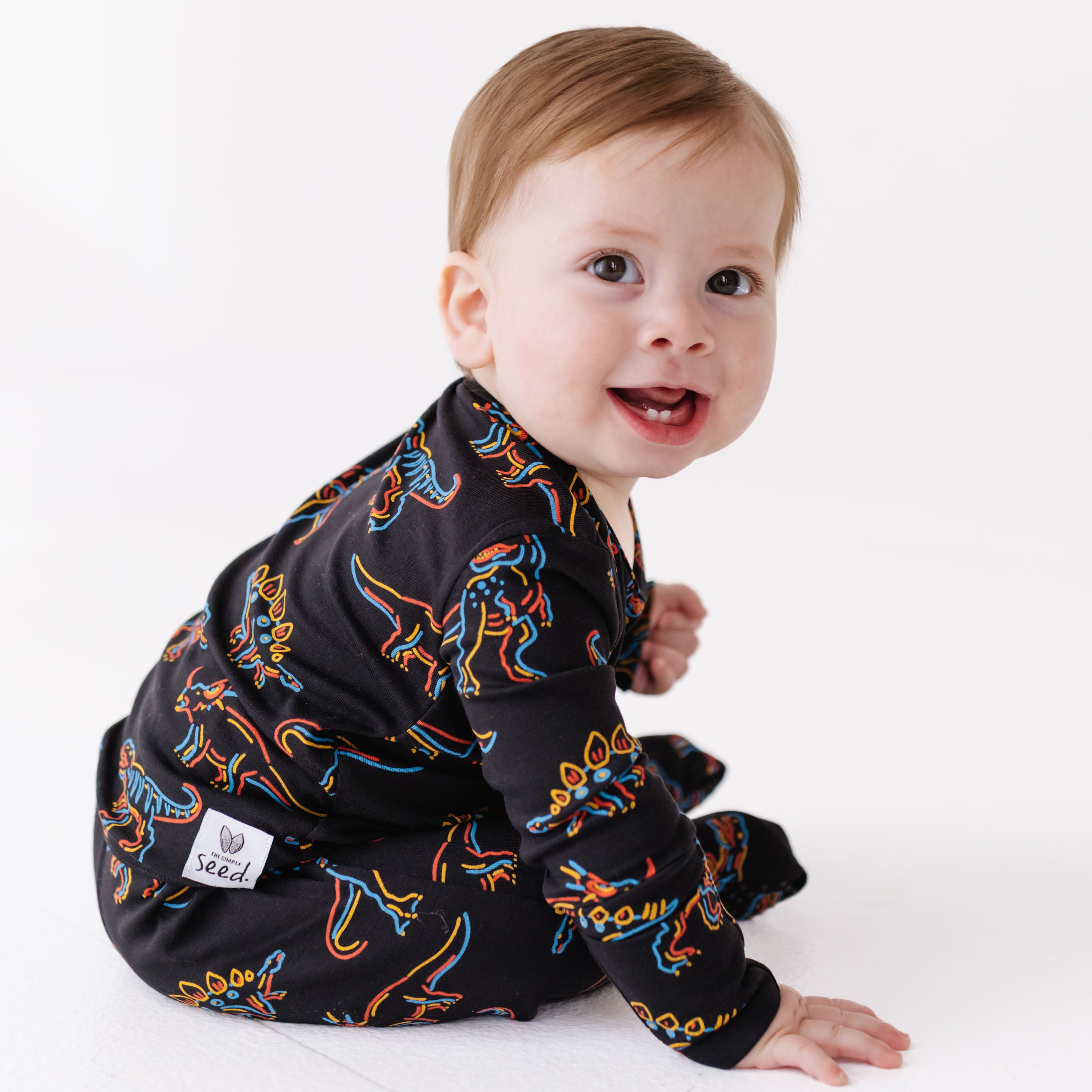 Baby wearing a black dinosaur print onesie on a white background