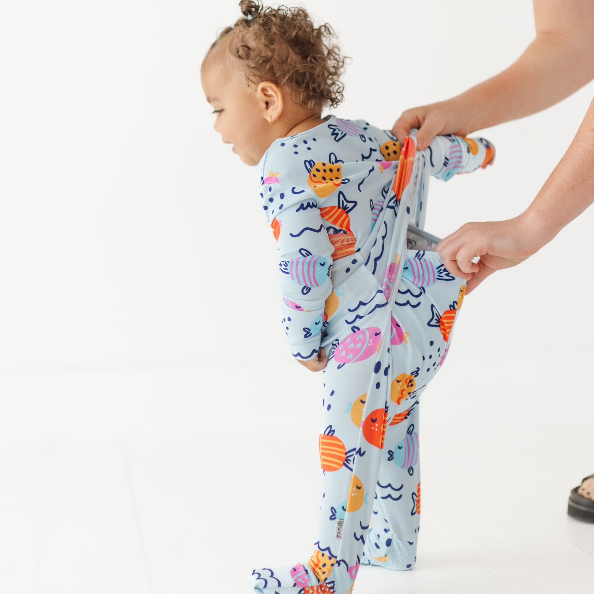 Child wearing a colorful onesie with sea-themed design, standing on a white background.