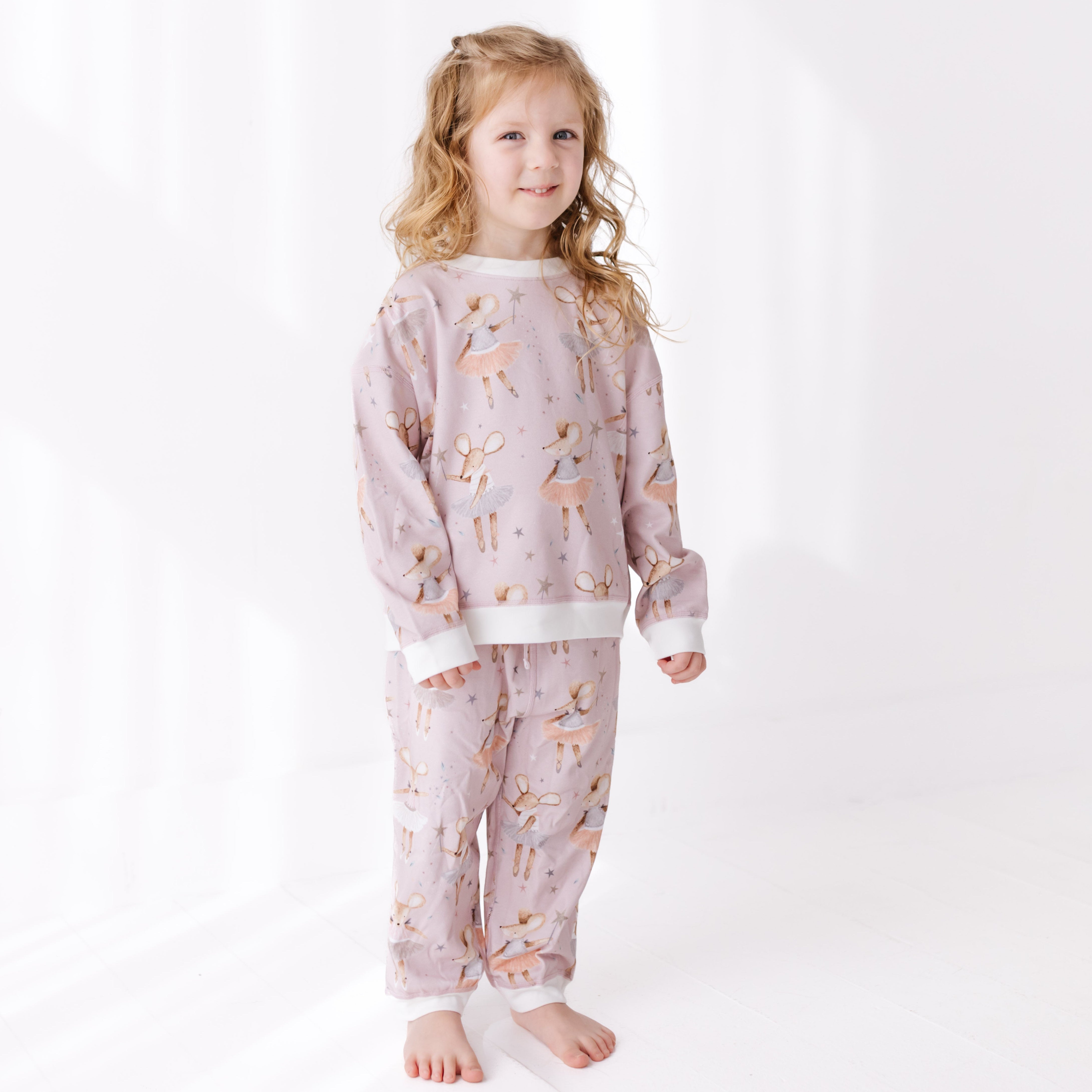 Young girl wearing a light pink sweat set with dancing mouse pattern on a white background