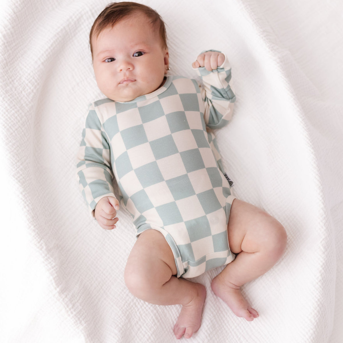 Baby wearing a checkered onesie on a white blanket
