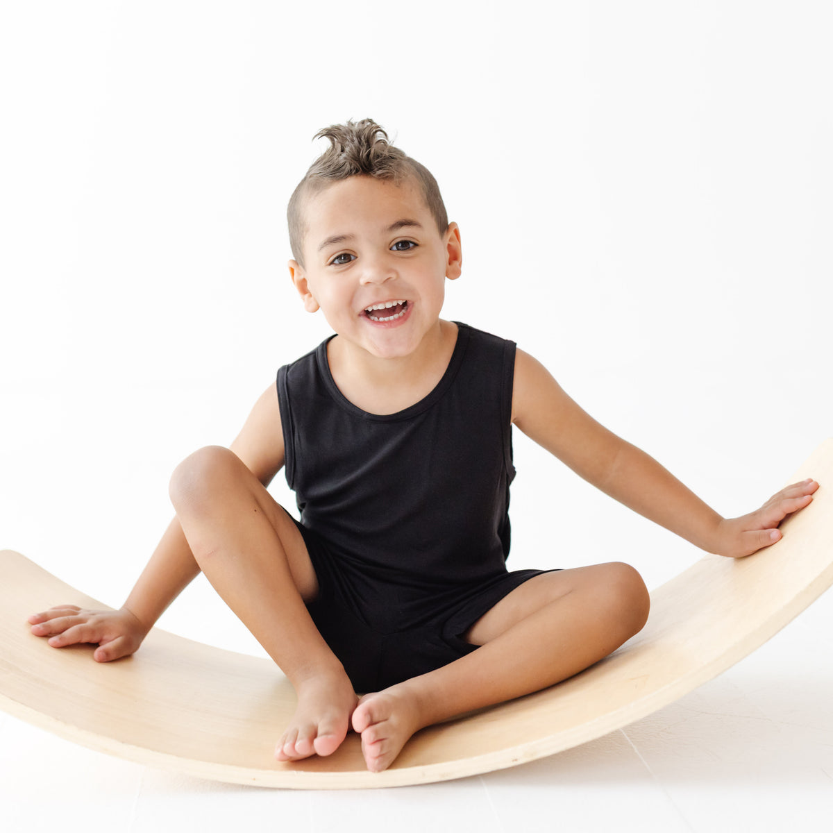 Child sitting on a wooden balance board with a white background