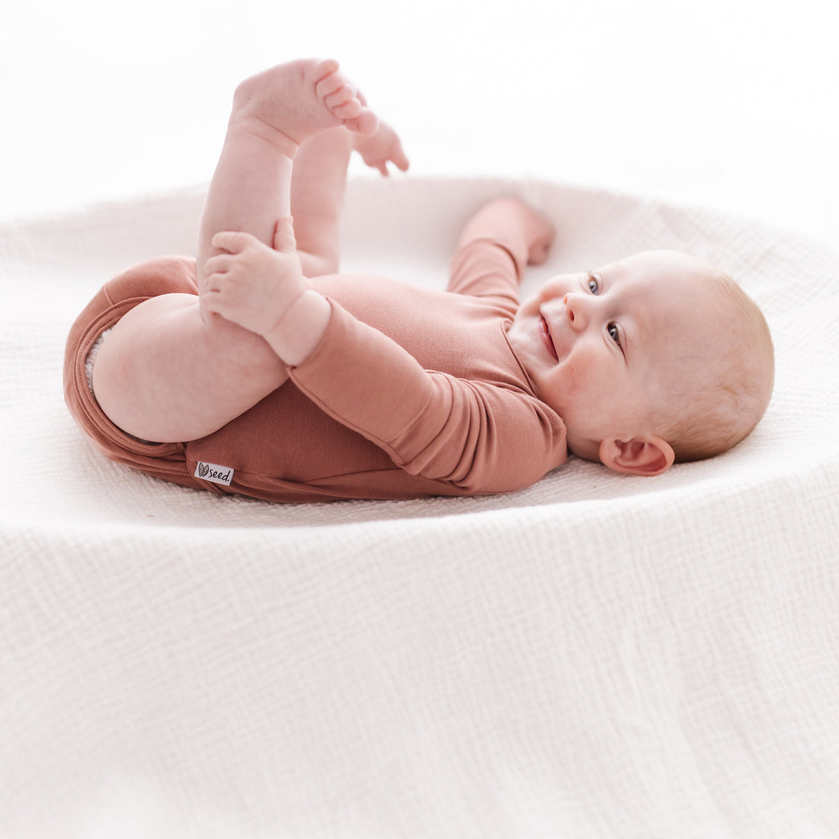 Baby in a pink outfit lying on a white blanket