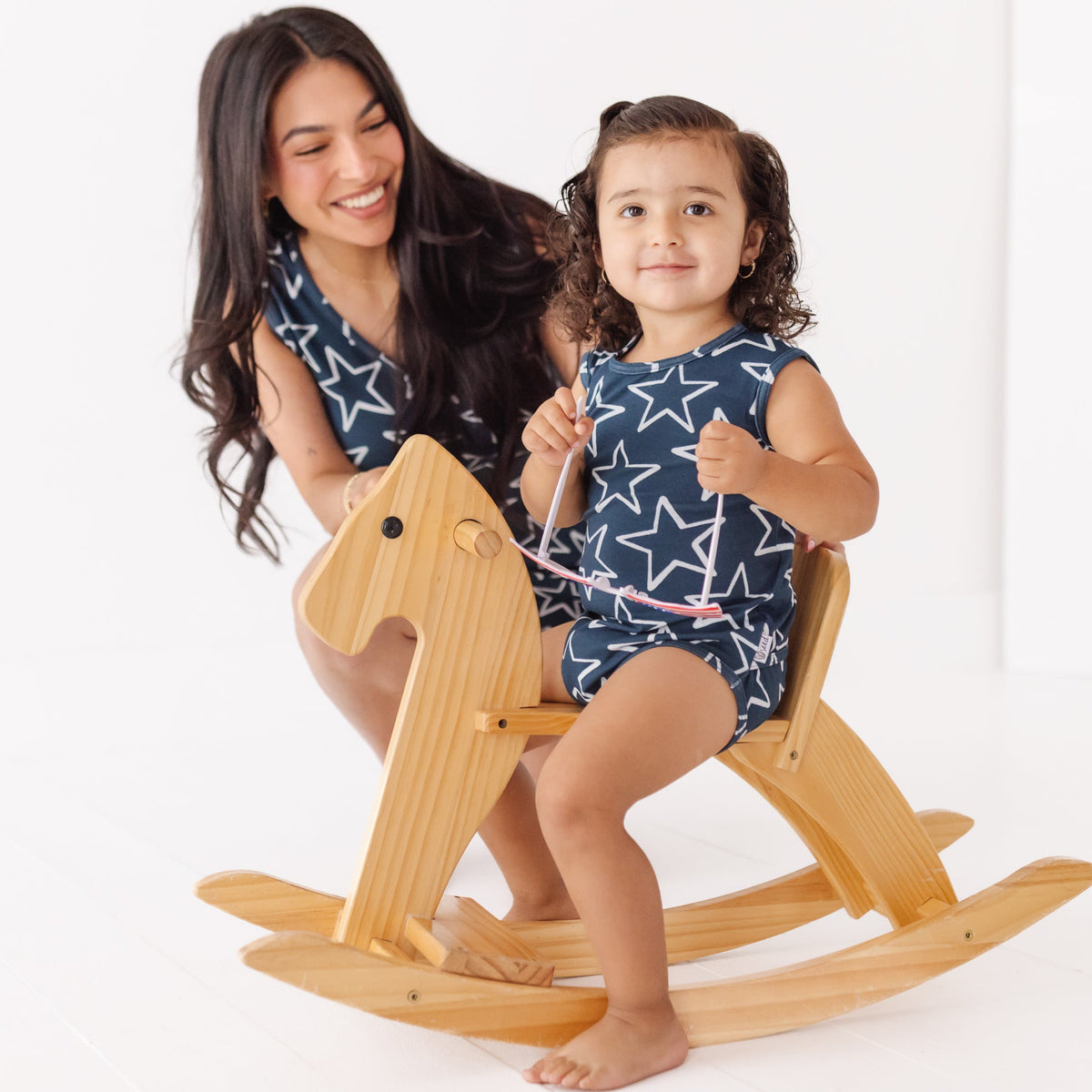 Woman and child in matching star-patterned outfits with a wooden rocking horse on a white background