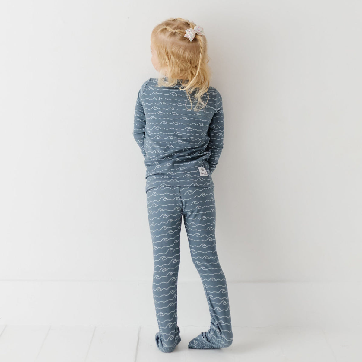 A girl stand on white floors wearing blue pajama set with waves on it.