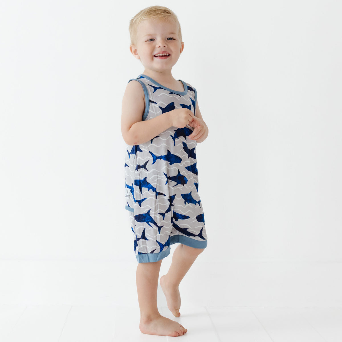 Child wearing a blue and gray shark-patterned romper on a white background