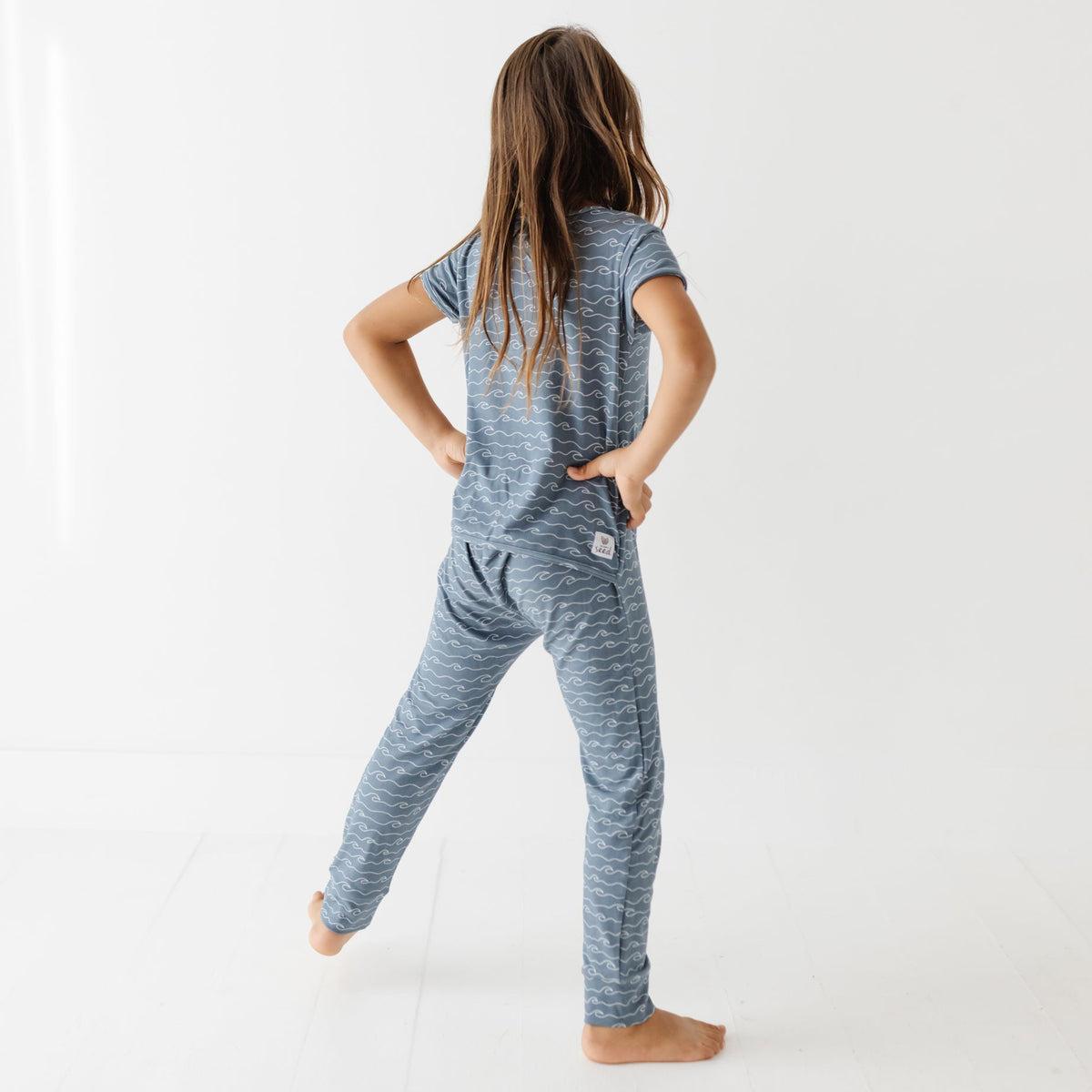 Kid stand on white floor wearing blue romper with waves.