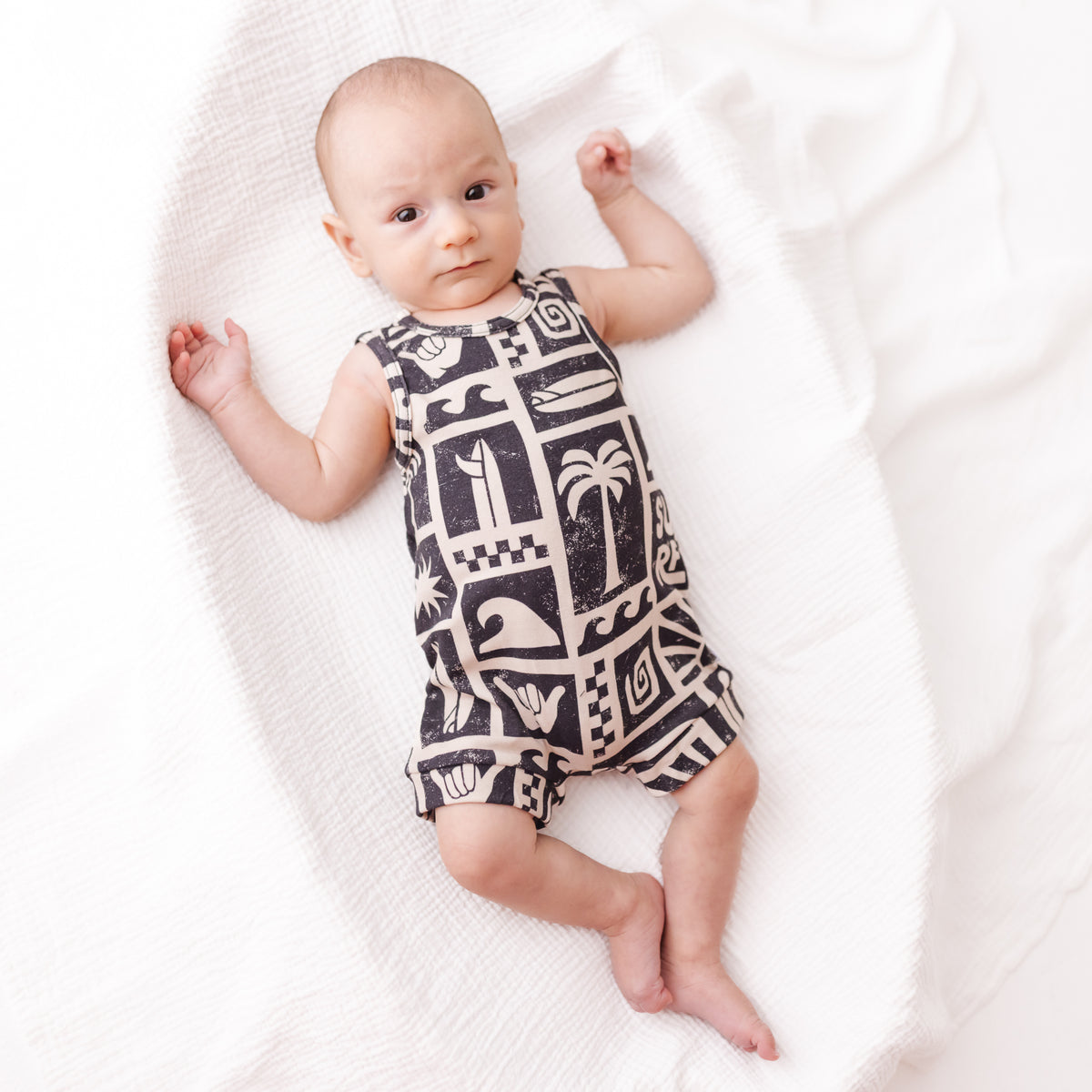 Baby wearing a black and white patterned romper on a white blanket