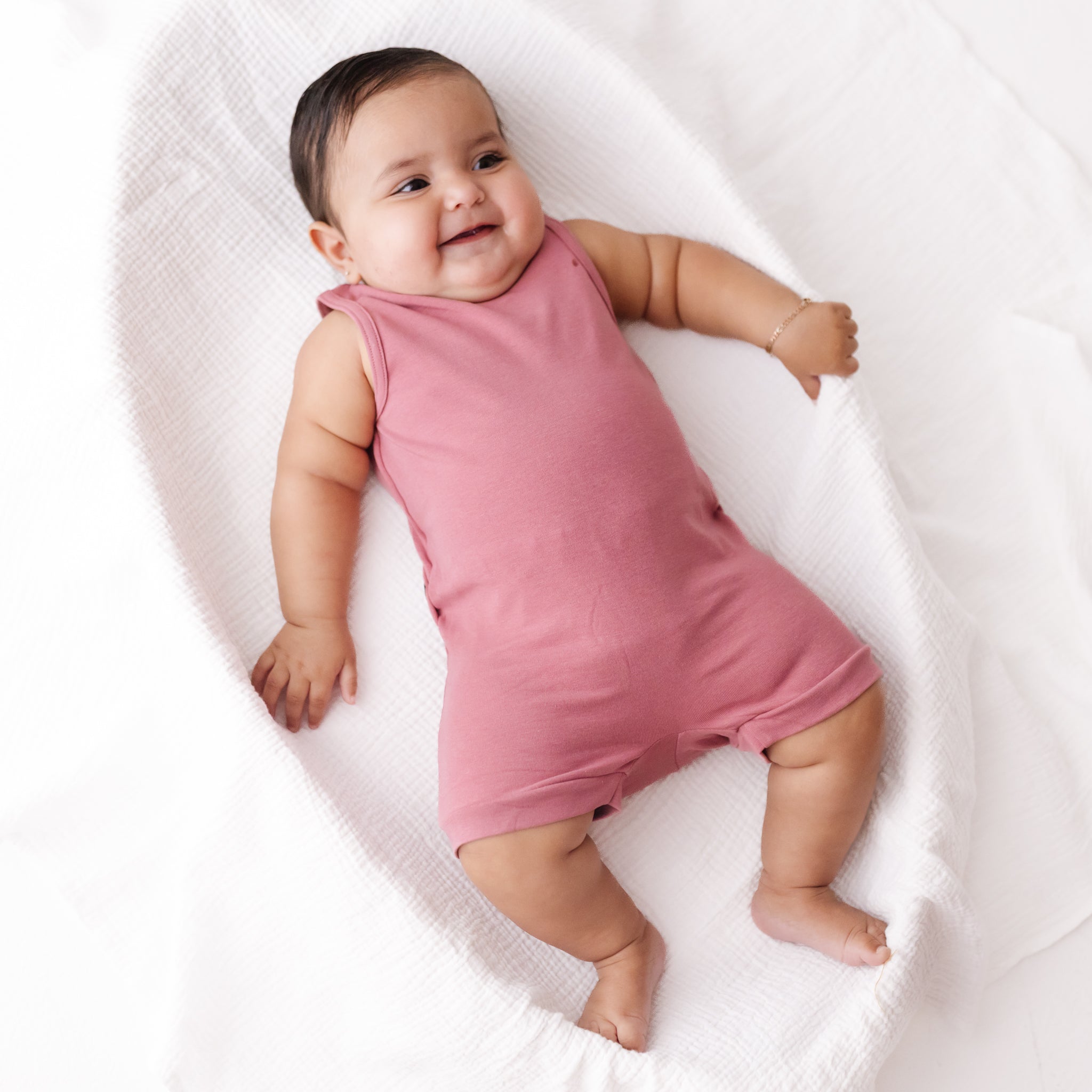 Baby wearing a pink romper lying on a white blanket