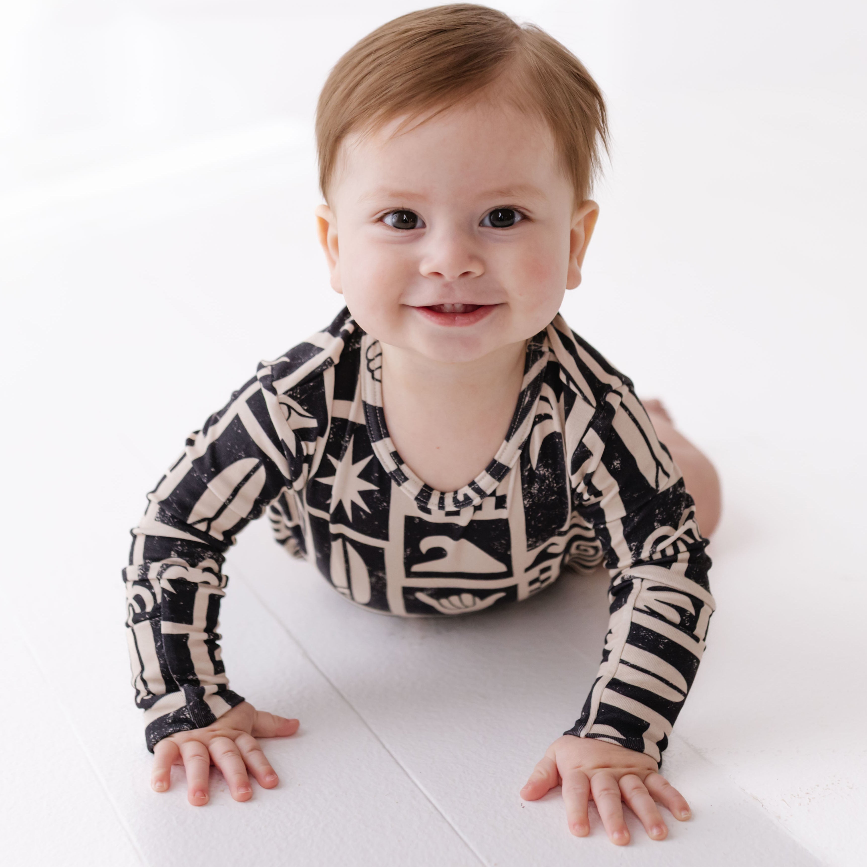 Baby wearing a patterned onesie on a white floor