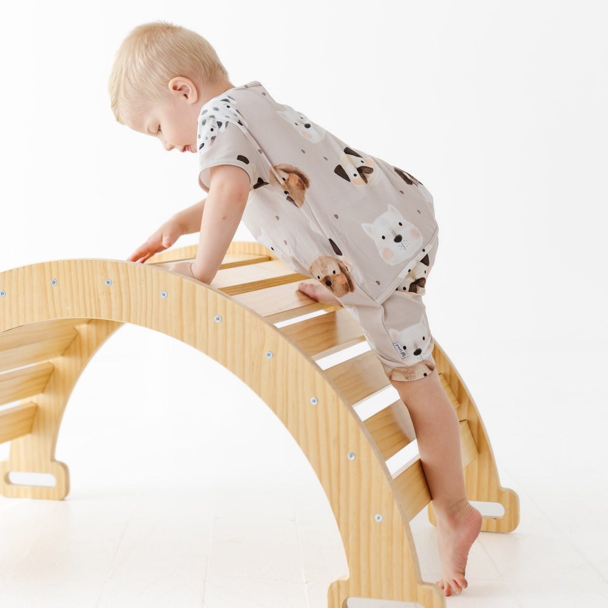 Child climbing on a wooden arch toy with a white background