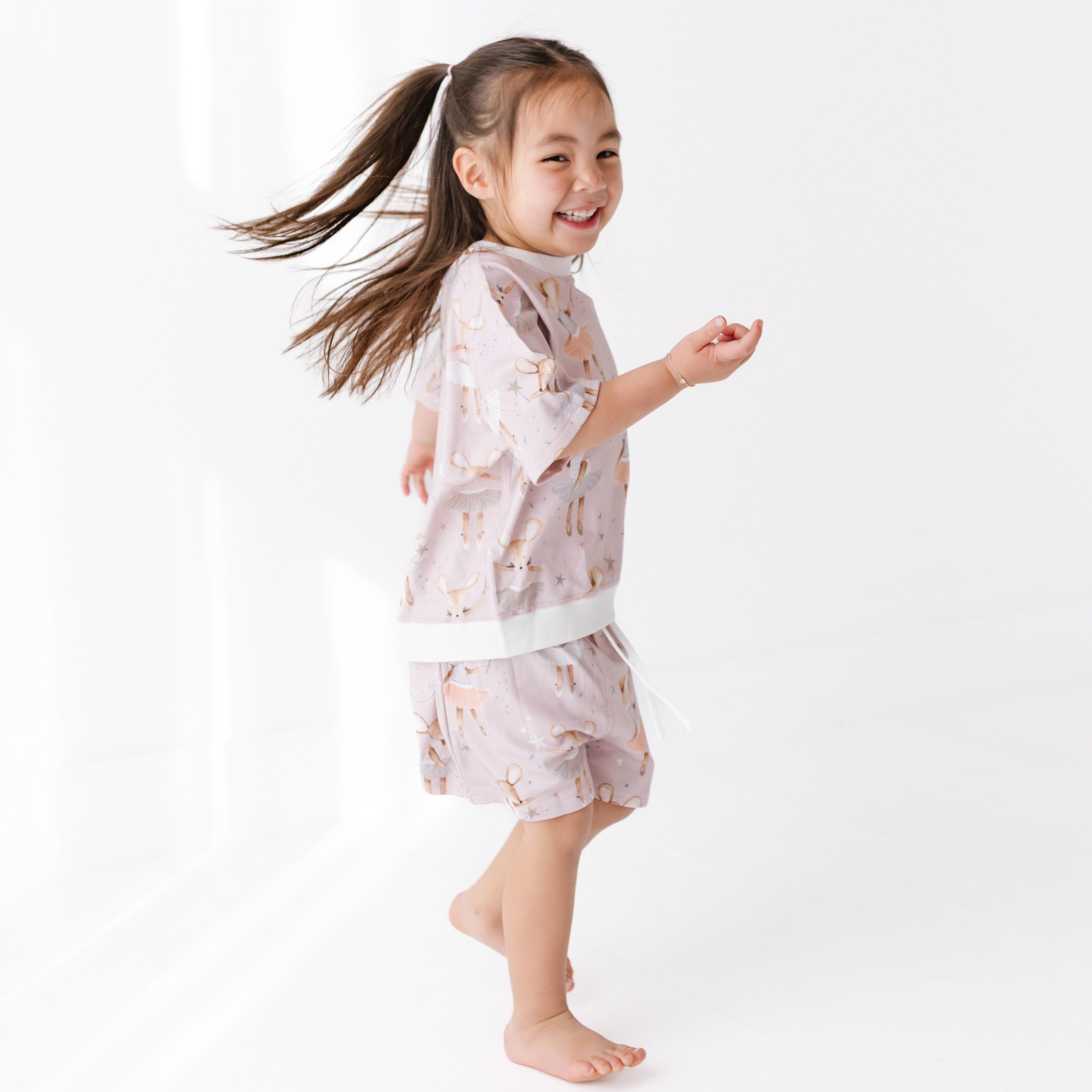 Child wearing a light pink outfit with dancing mice, standing on a white background