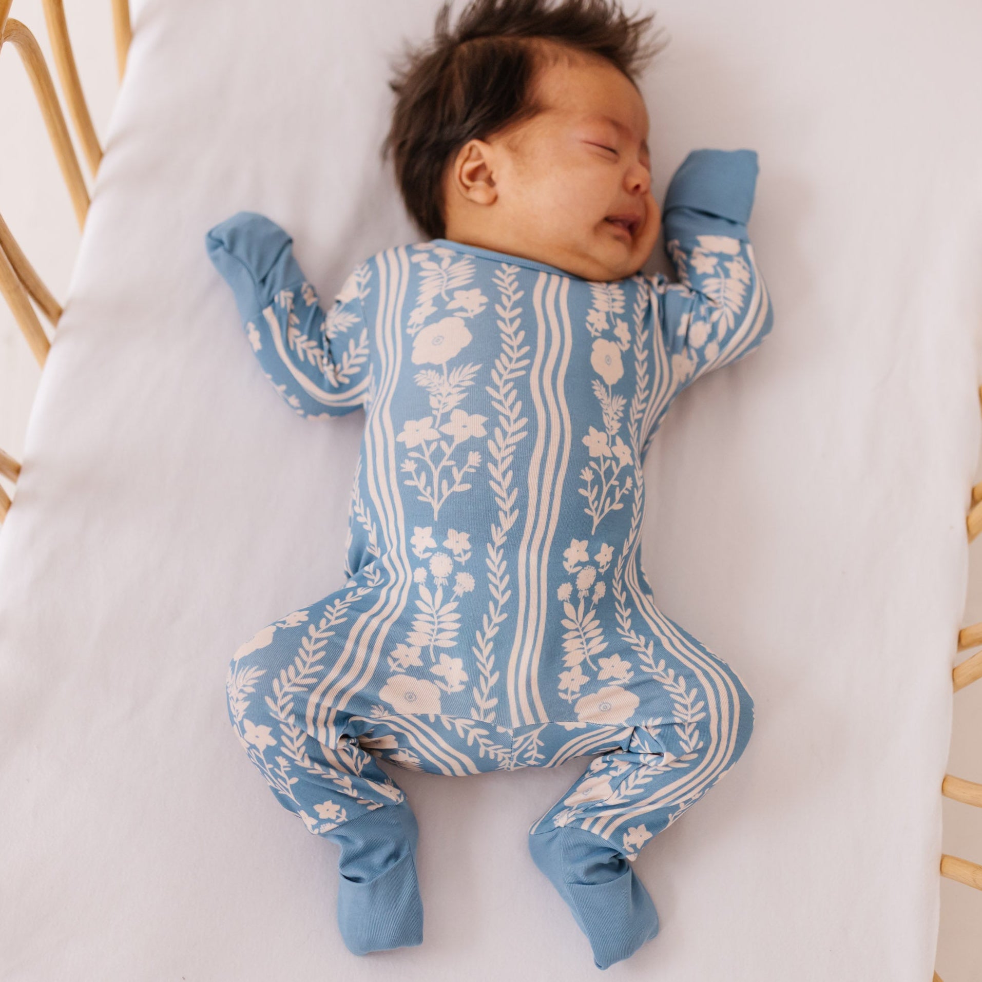 Newborn baby wearing a blue and white patterned onesie lying on a white cushion.