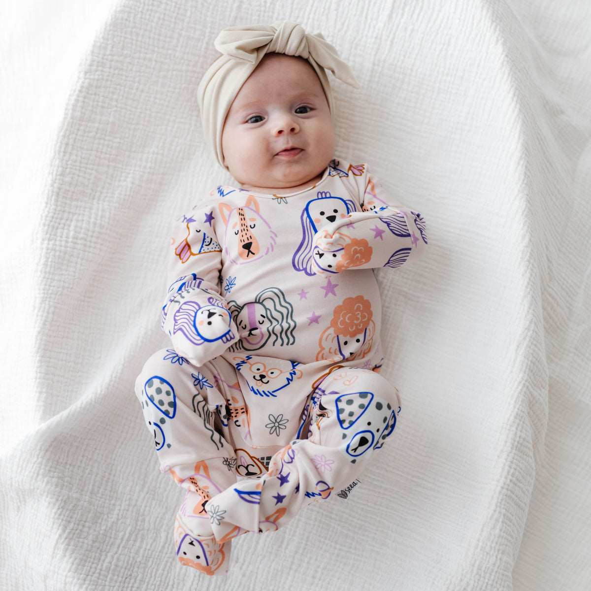 Baby wearing a colorful onesie with animal prints on a white blanket