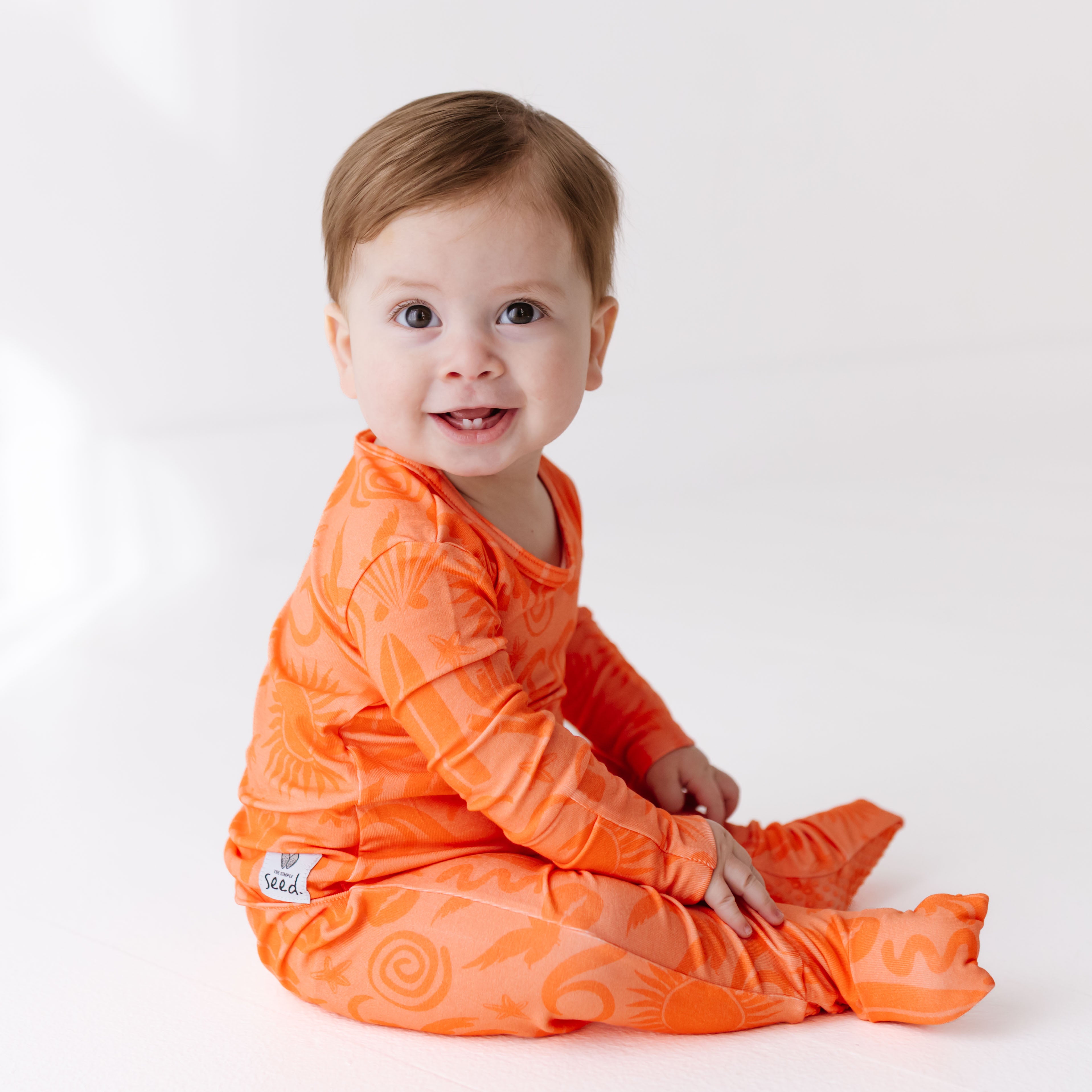 Baby wearing an orange outfit with a white background