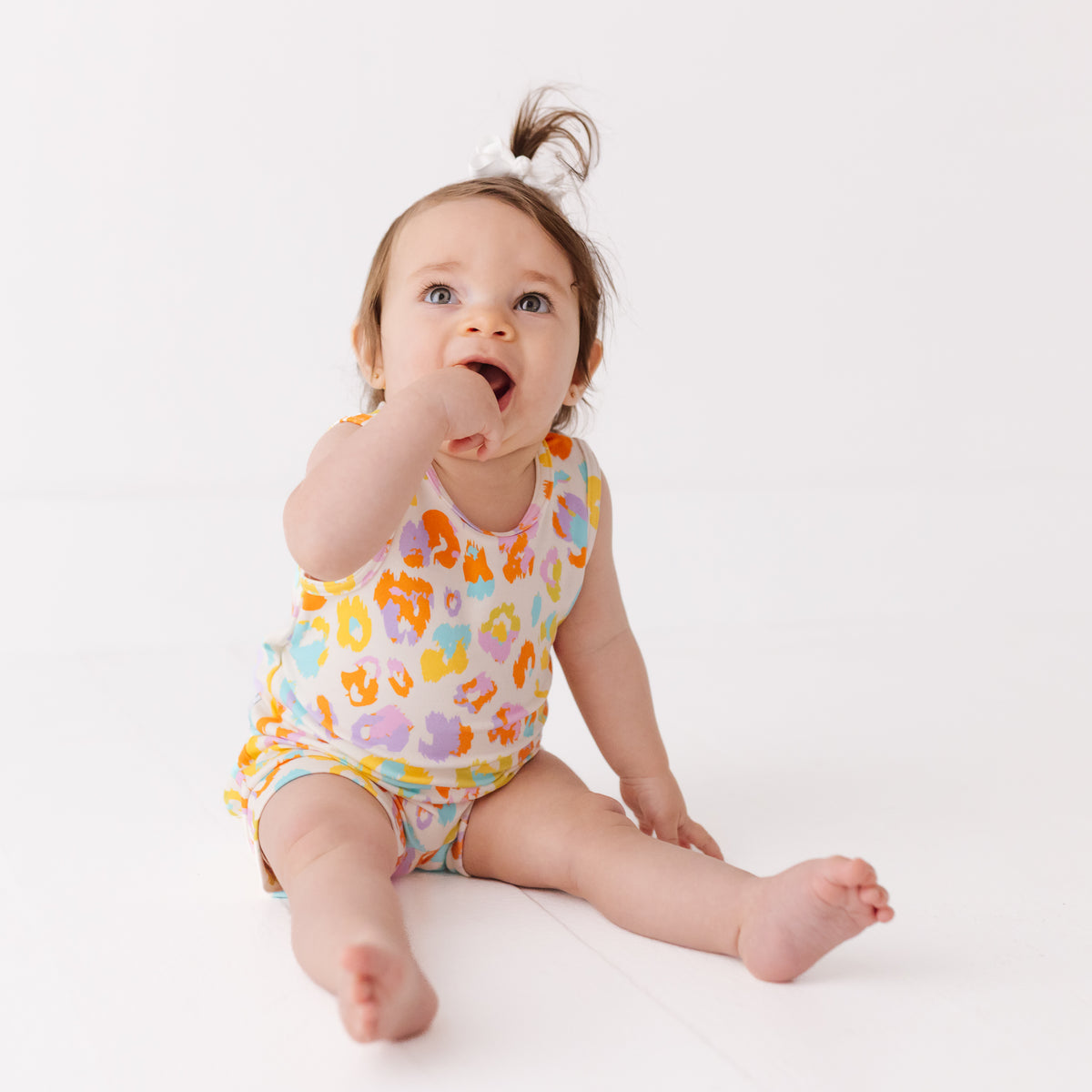 Baby wearing a colorful onesie sitting on a white background