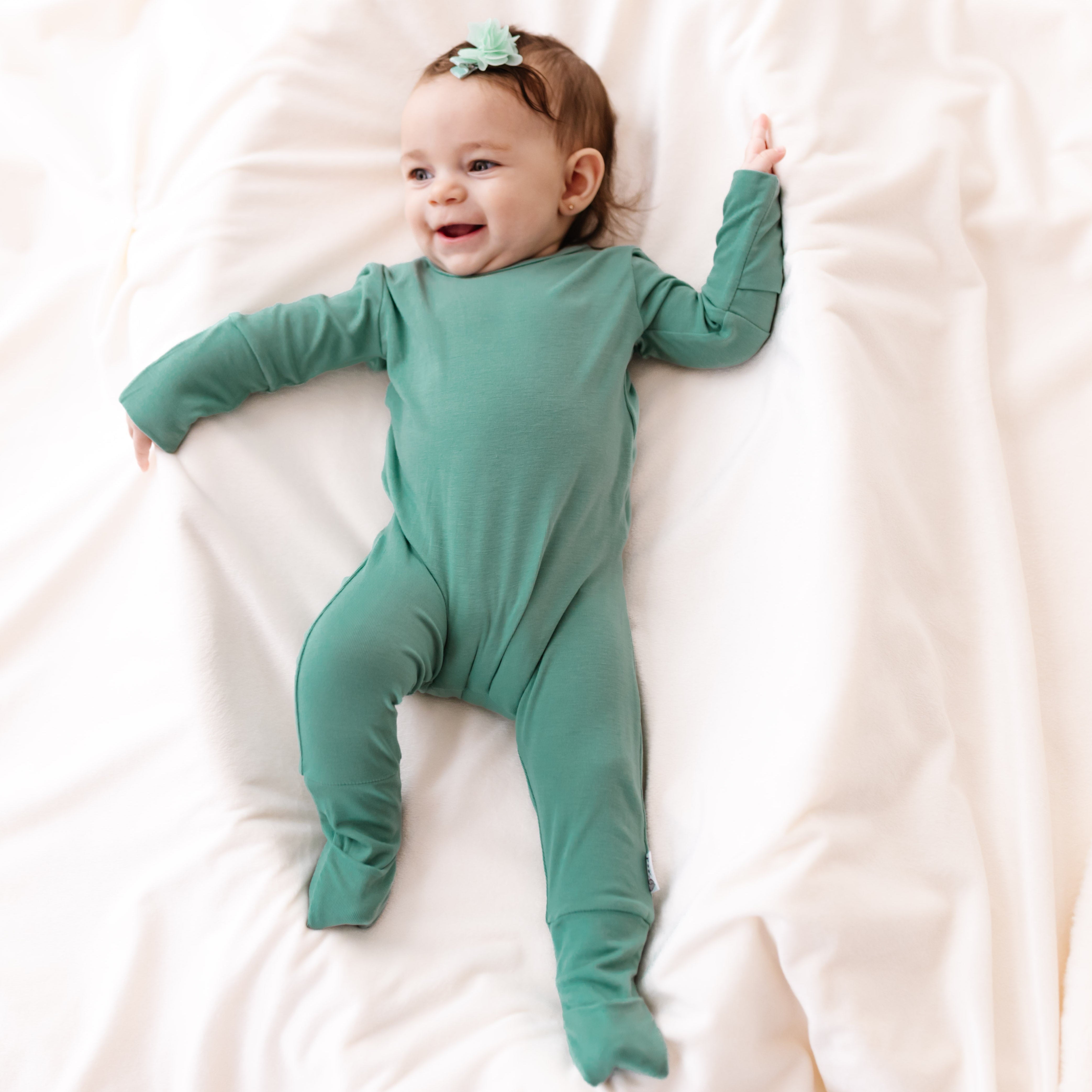 Baby in a green onesie lying on a white blanket