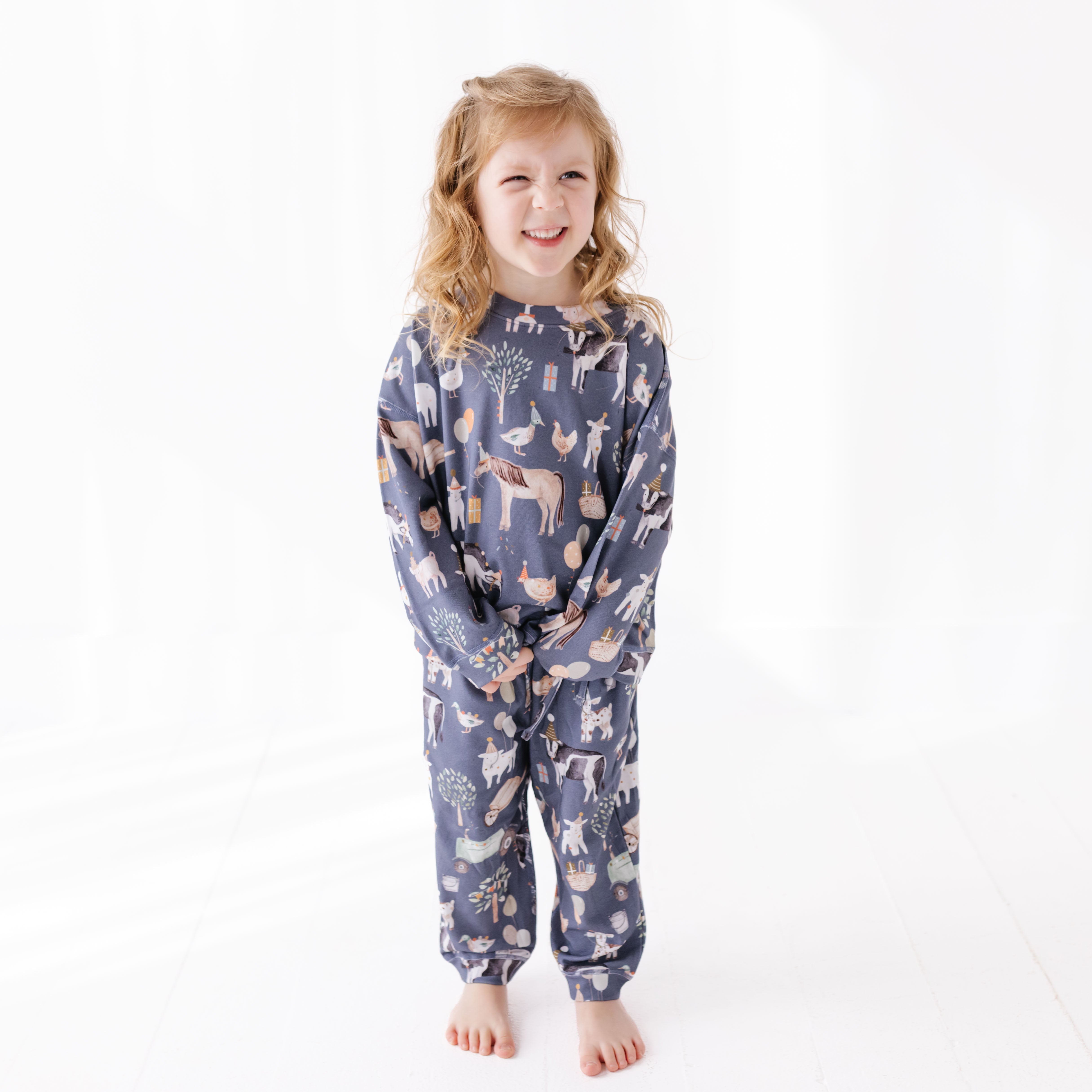 Child wearing a blue sweat set with party farm animal prints on a white background