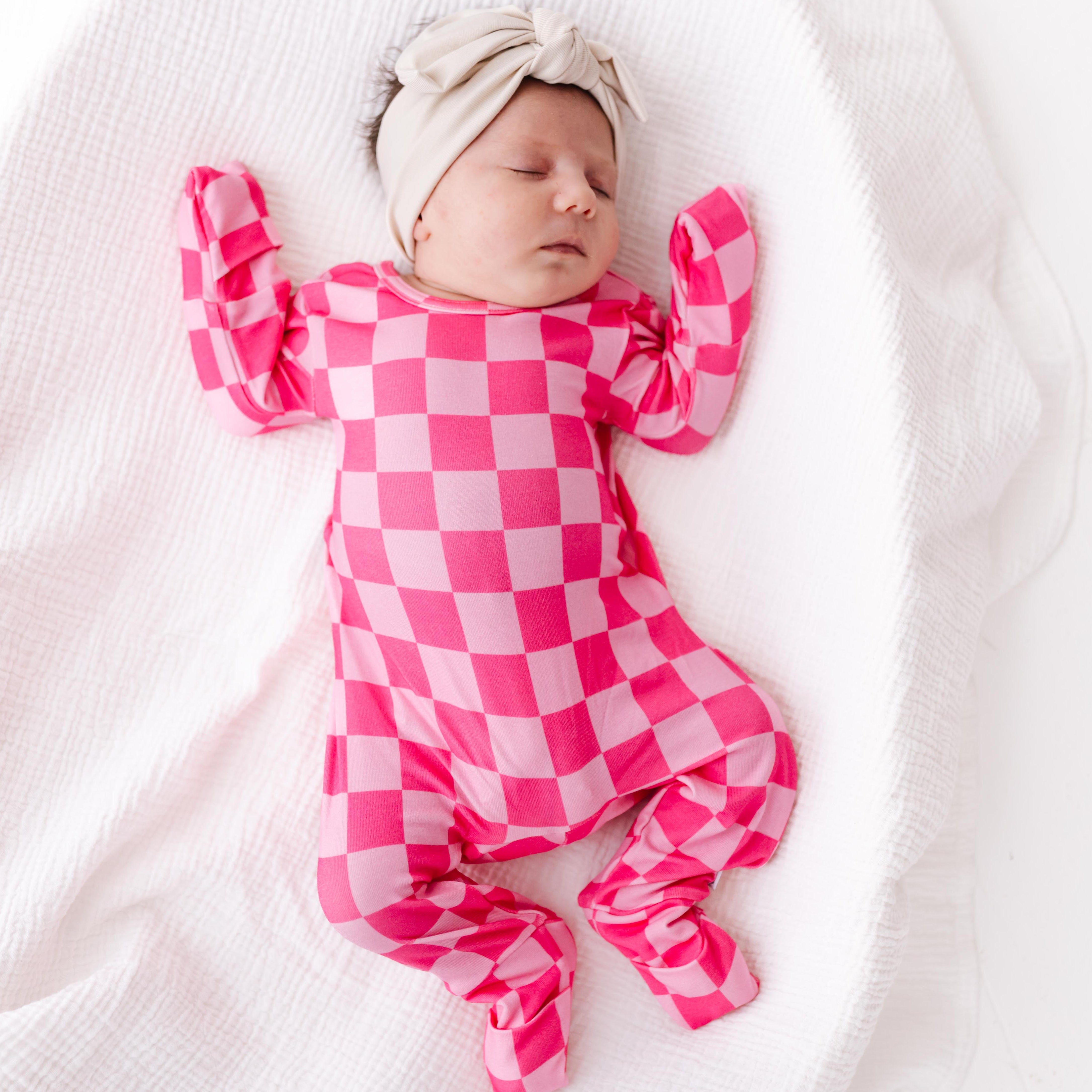 Newborn baby in a pink and light pink checkered outfit lying on a white blanket