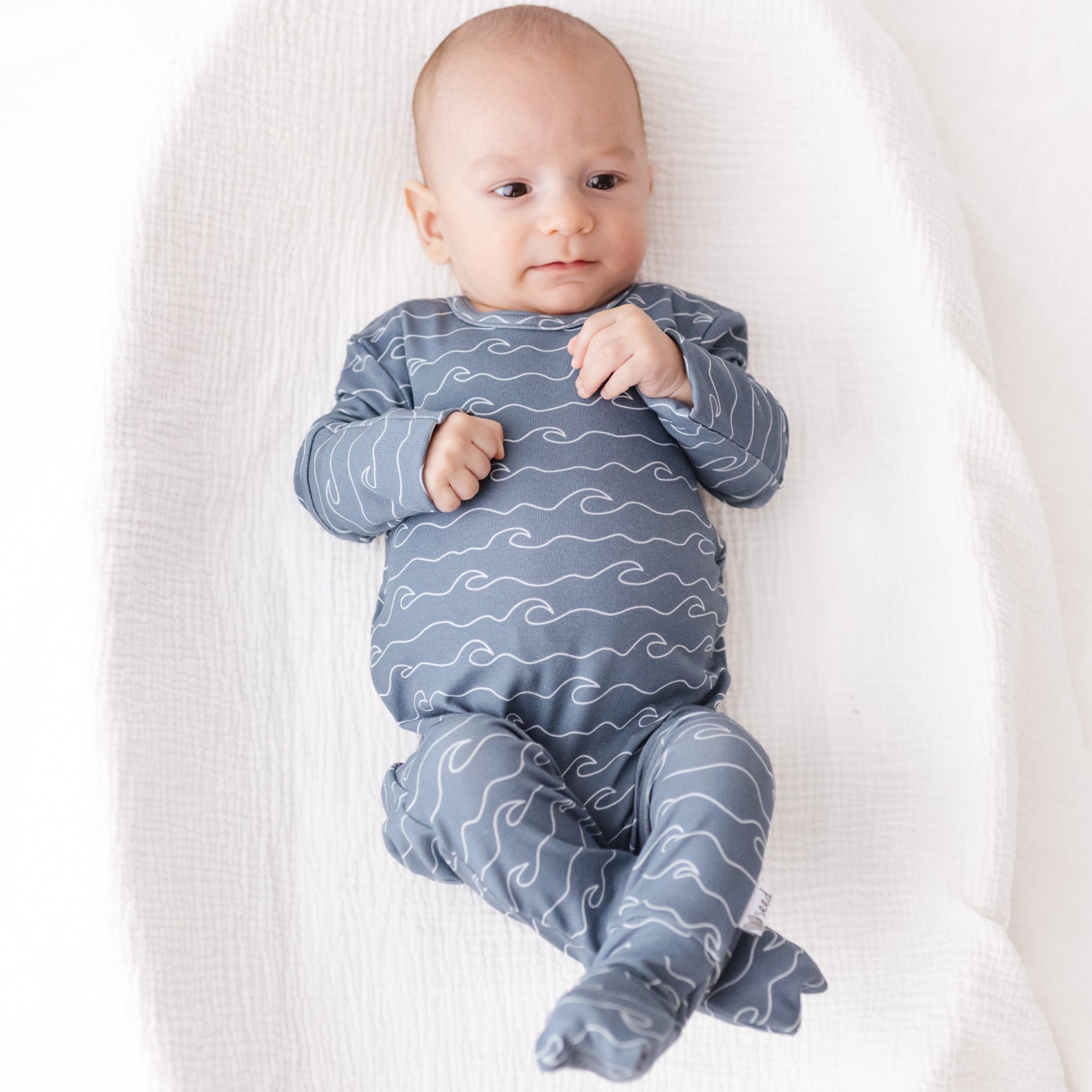 Baby wearing a blue wave-patterned outfit on a white blanket