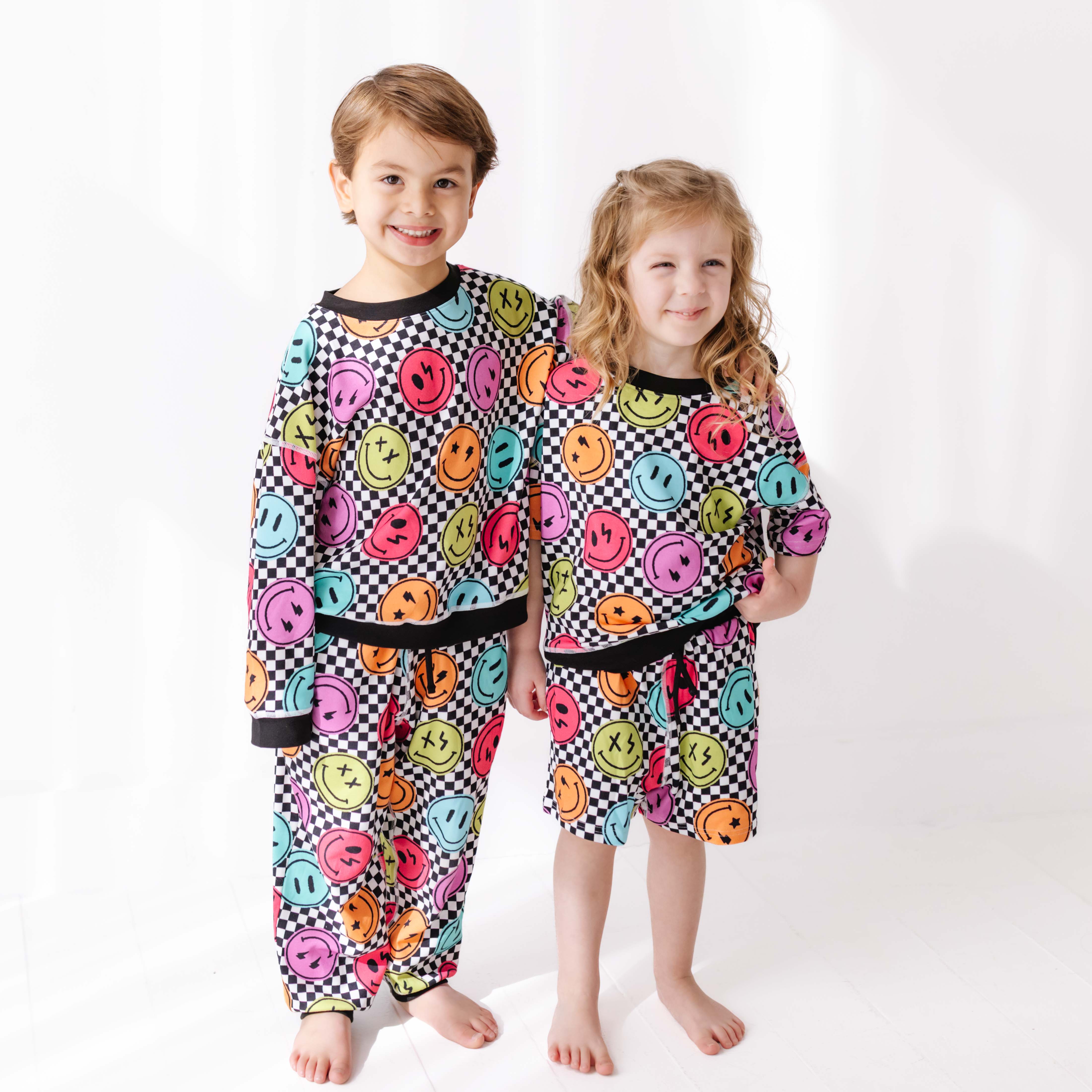 Two children wearing colorful sweatsuit with smiley face pattern on a white background