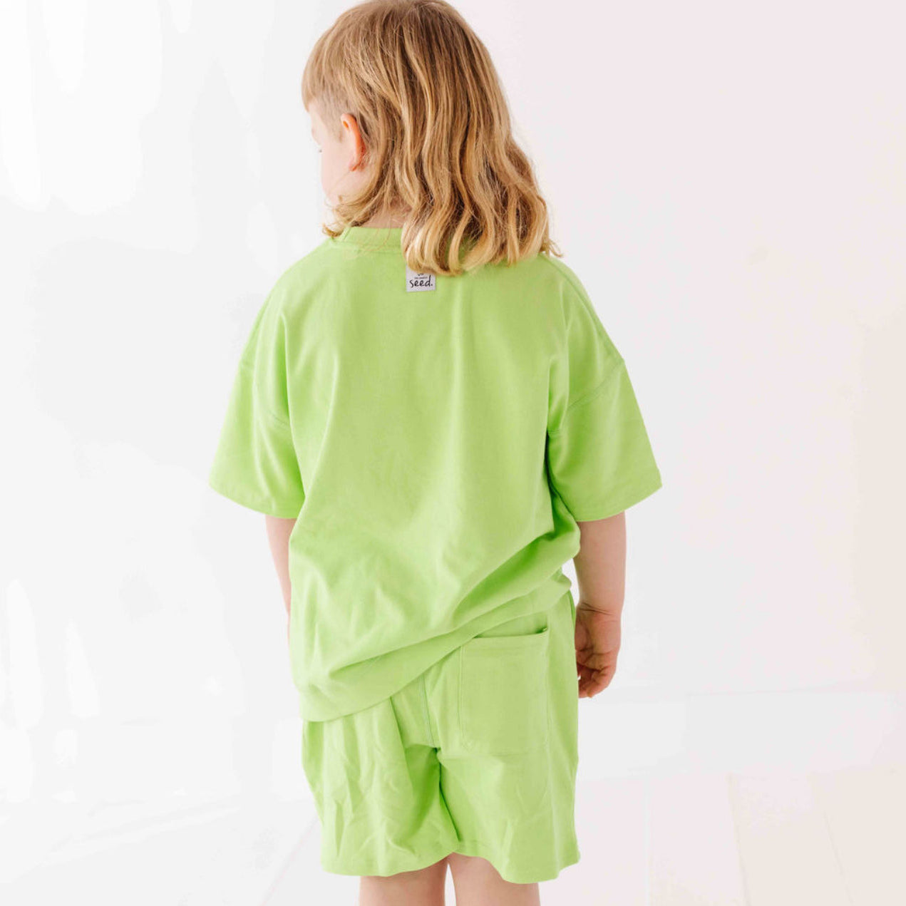Child wearing a light green outfit with a visible brand label on a white background