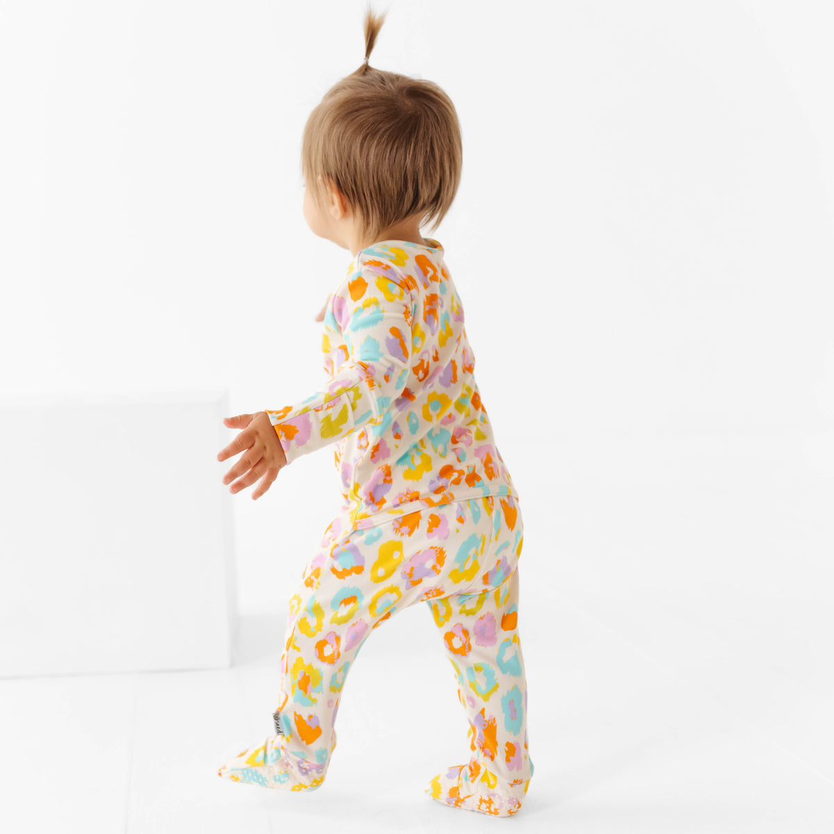 Child wearing a colorful leopard print onesie on a white background