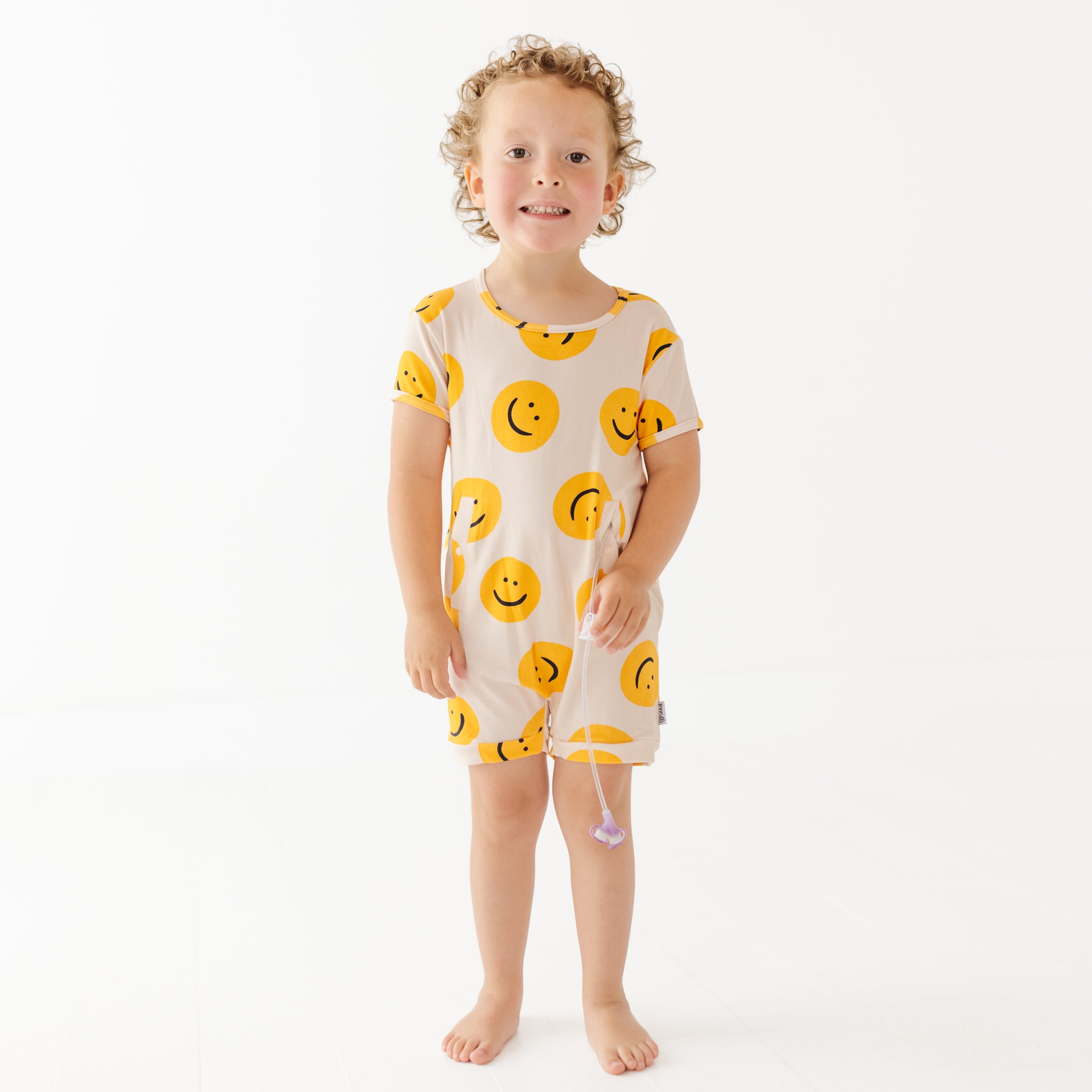 Child wearing a white outfit with yellow smiley face patterns on a white background