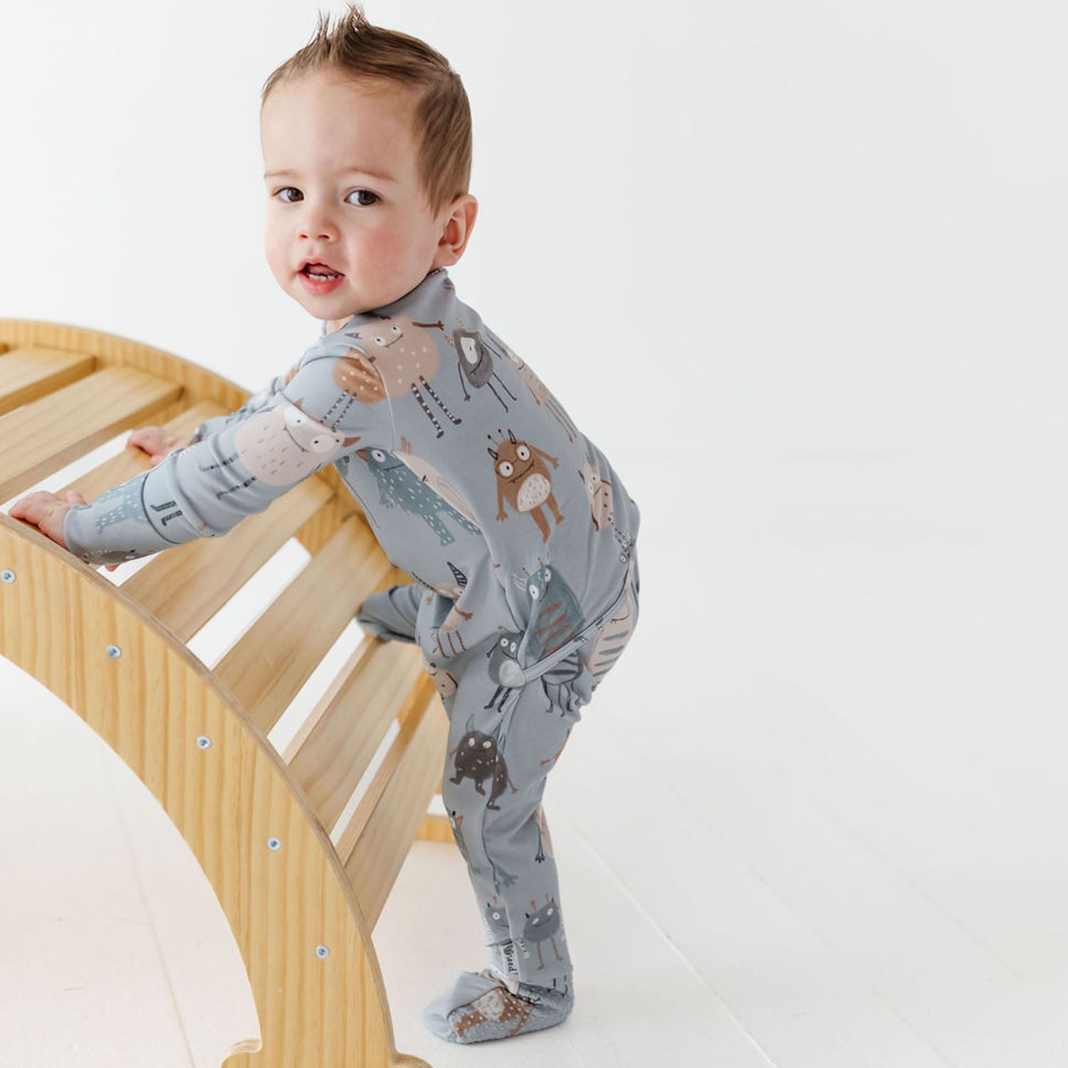 Baby in a gray onesie with animal pattern standing on a wooden arch
