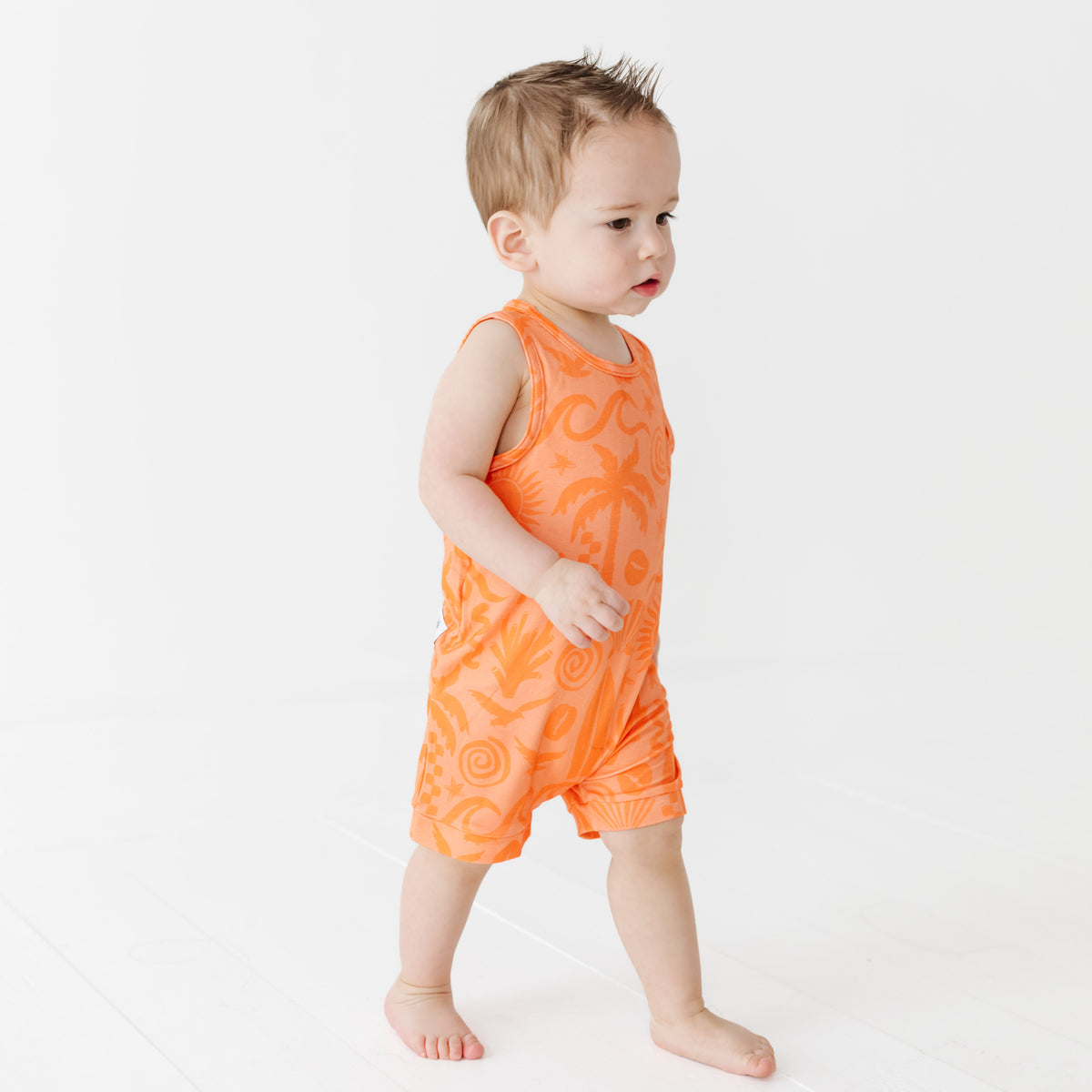 Child wearing an orange sleeveless romper on a white background
