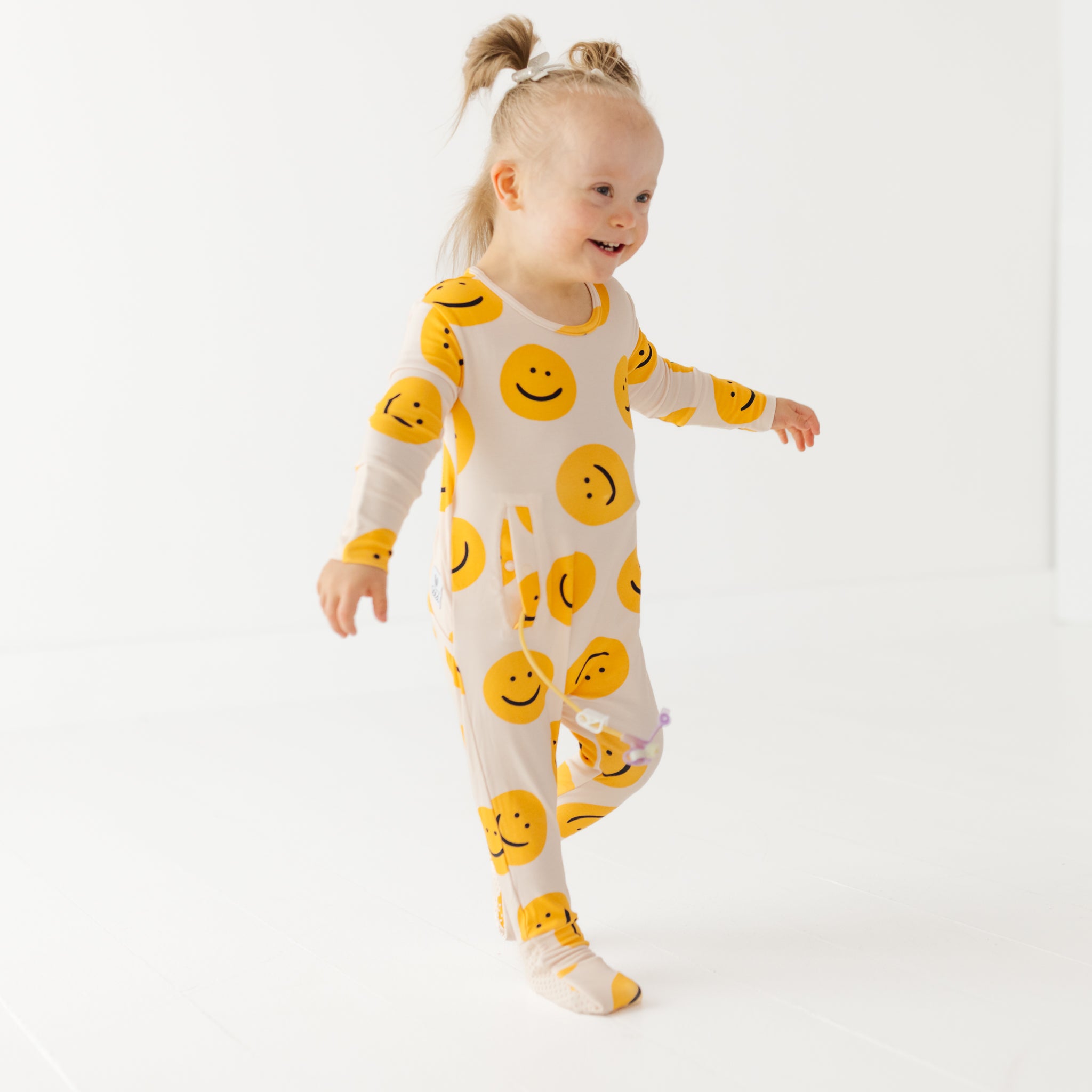 Child wearing a white onesie with yellow smiley face patterns on a plain background