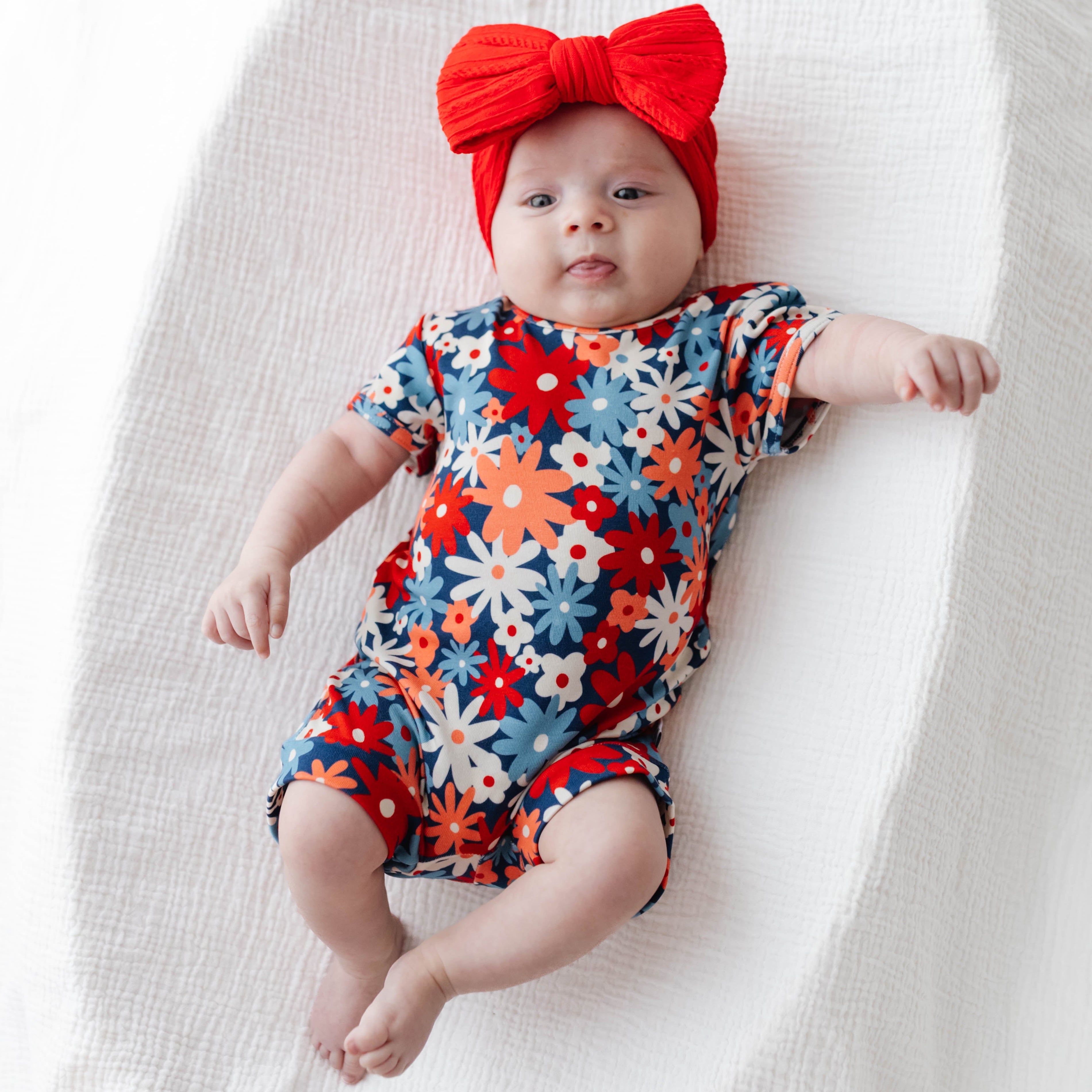 Baby wearing a colorful floral onesie and red bow headband on a white background