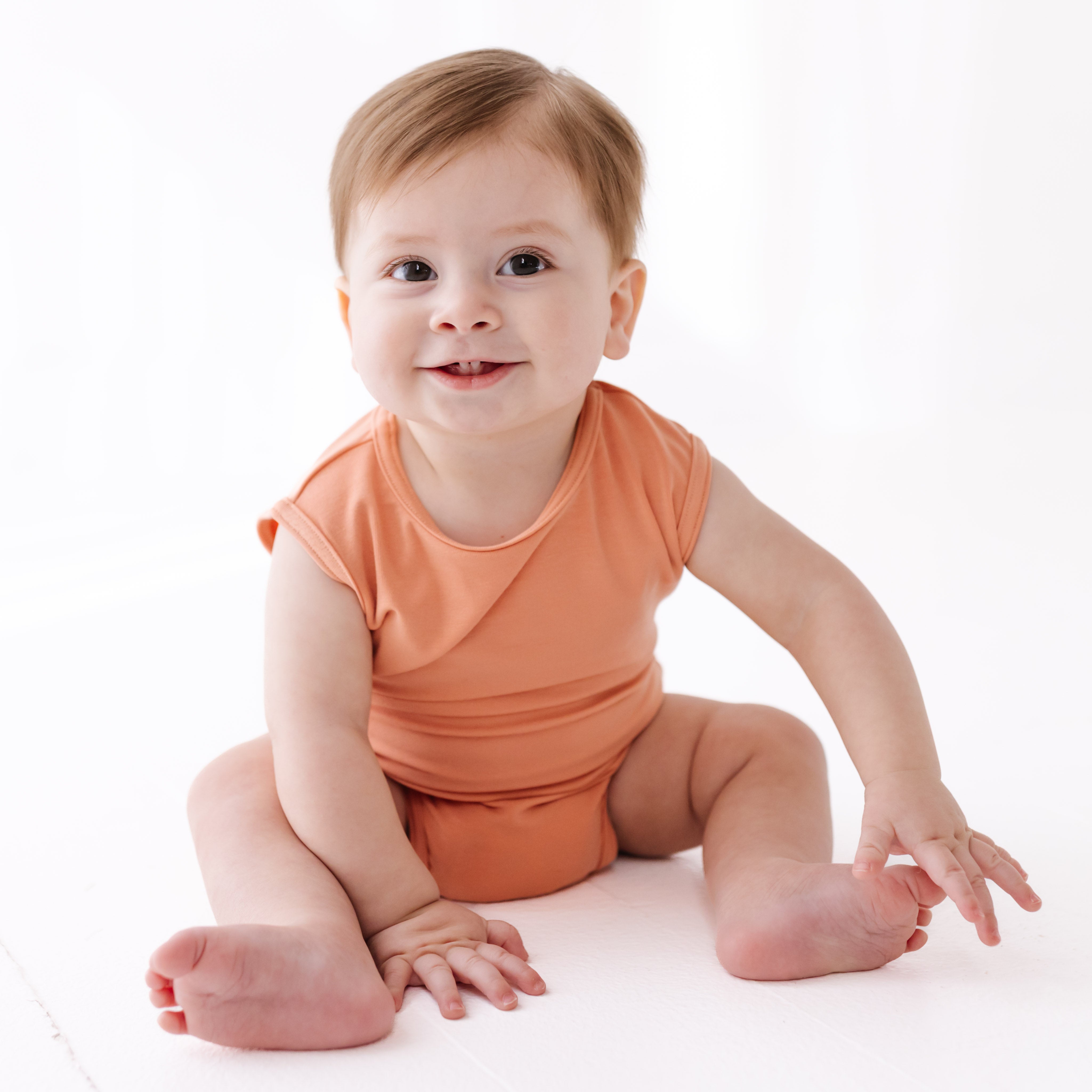 Baby wearing an orange outfit sitting on a white background