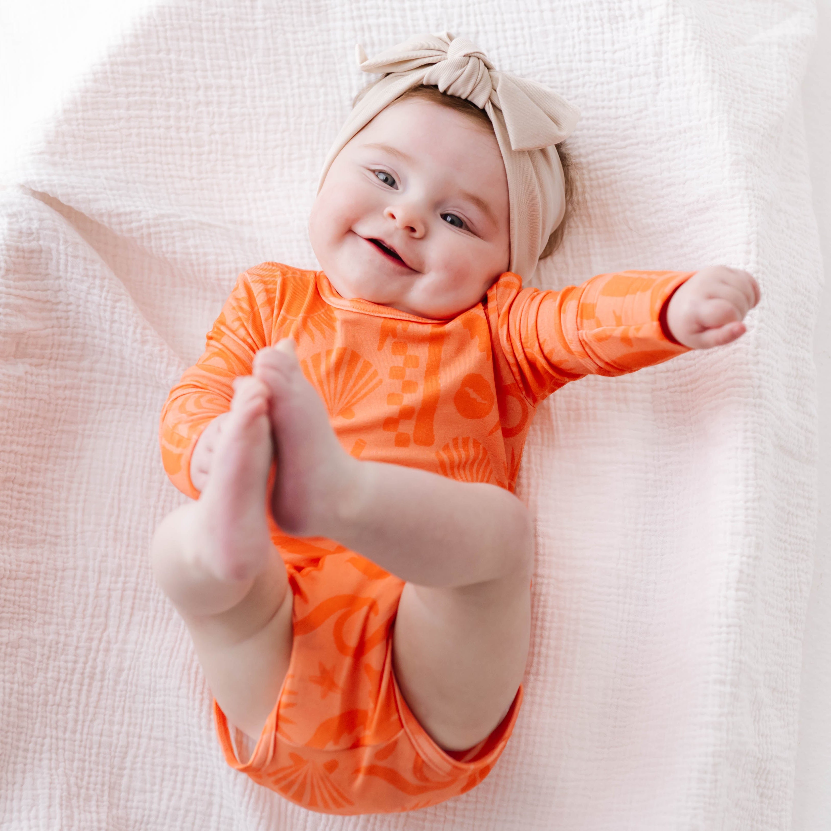 Baby in an orange onesie and headband lying on a white blanket