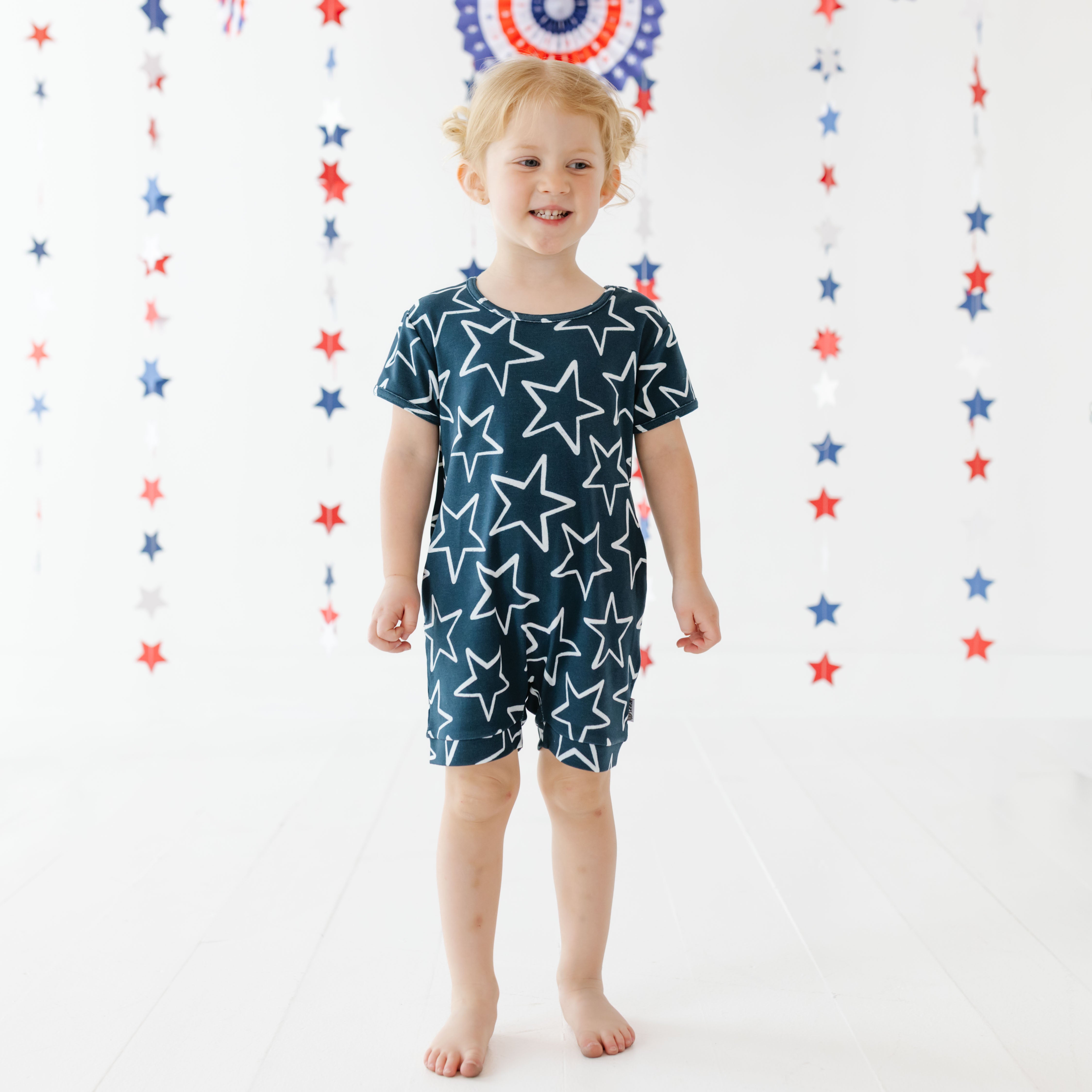 Child wearing a navy blue romper with white star pattern against a decorative star background