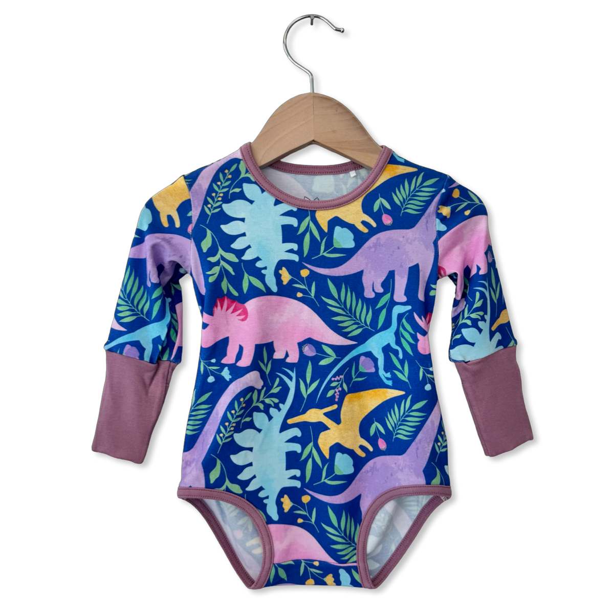 A baby long-sleeve bodysuit with a colorful dinosaur and leaf pattern, hanging on a wooden hanger against a white background.