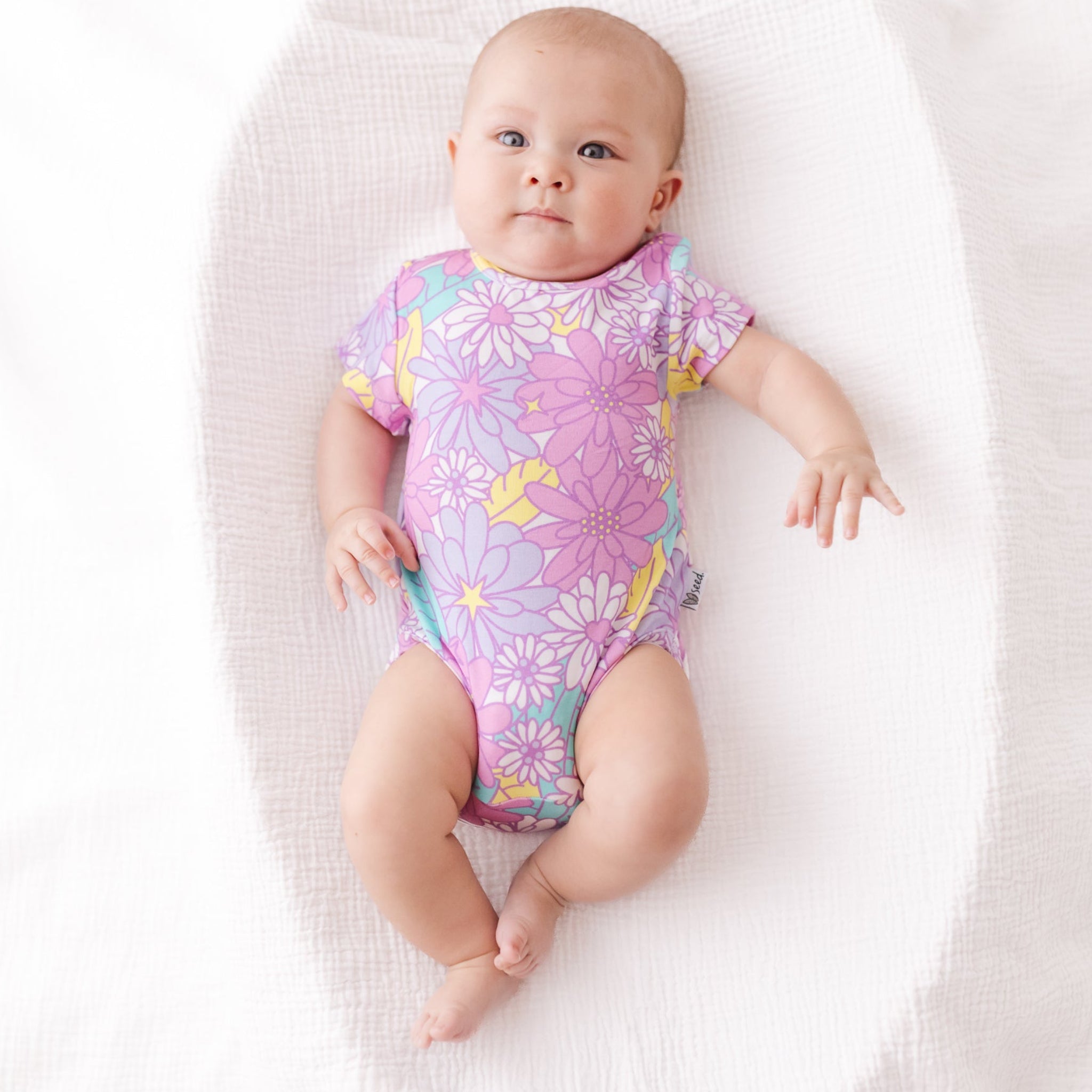 Baby wearing a colorful floral onesie on a white blanket